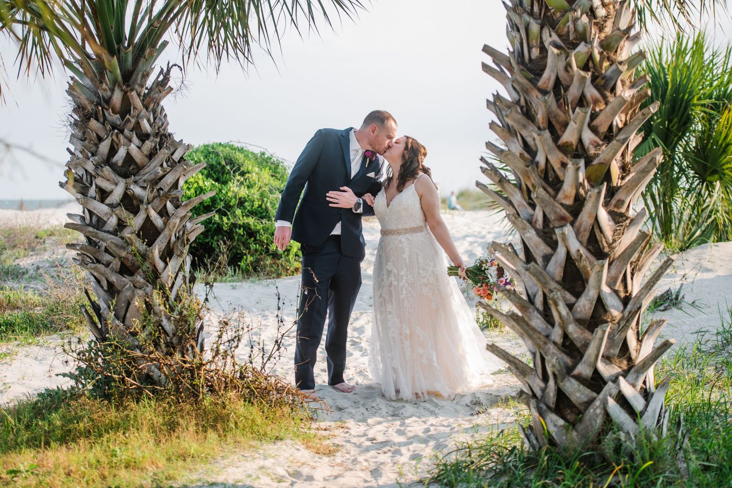 Palm trees frame a beachside wedding ceremony with white sand and ocean views.