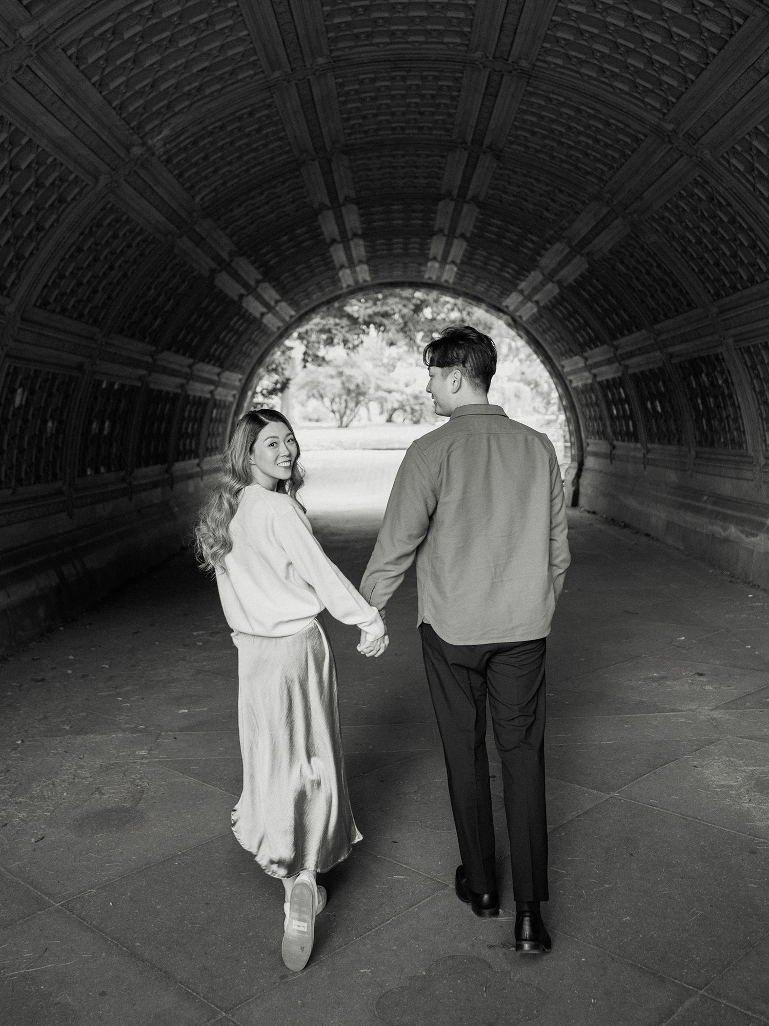 A romantic couple walks through an arched tunnel in black and white.