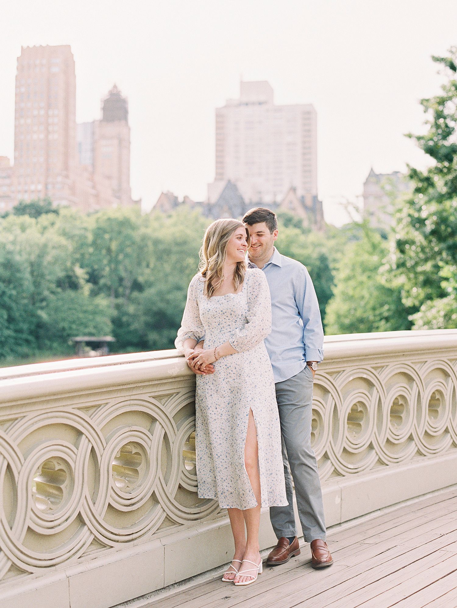 A couple shares intimate moments along an ornate stone balcony with a city skyline in the background.
