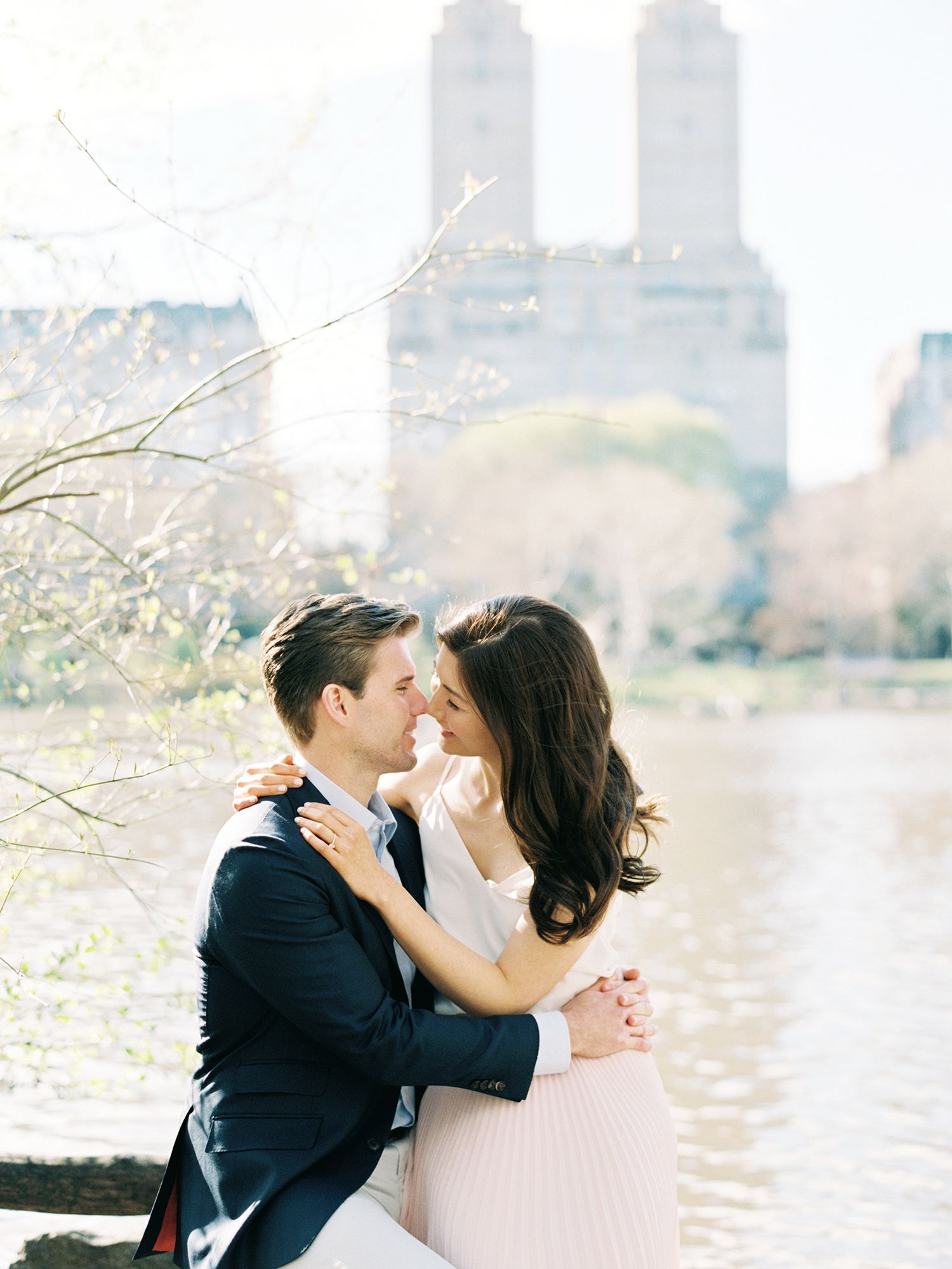 A romantic moment captured by the water with iconic city buildings in the background.