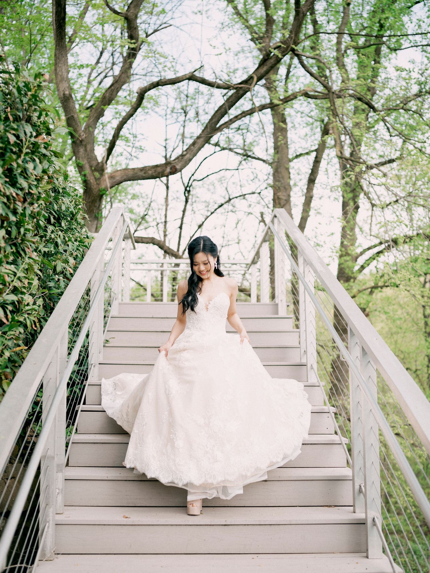 Bride in white dress walking up wooden outdoor stairs surrounded by spring greenery.