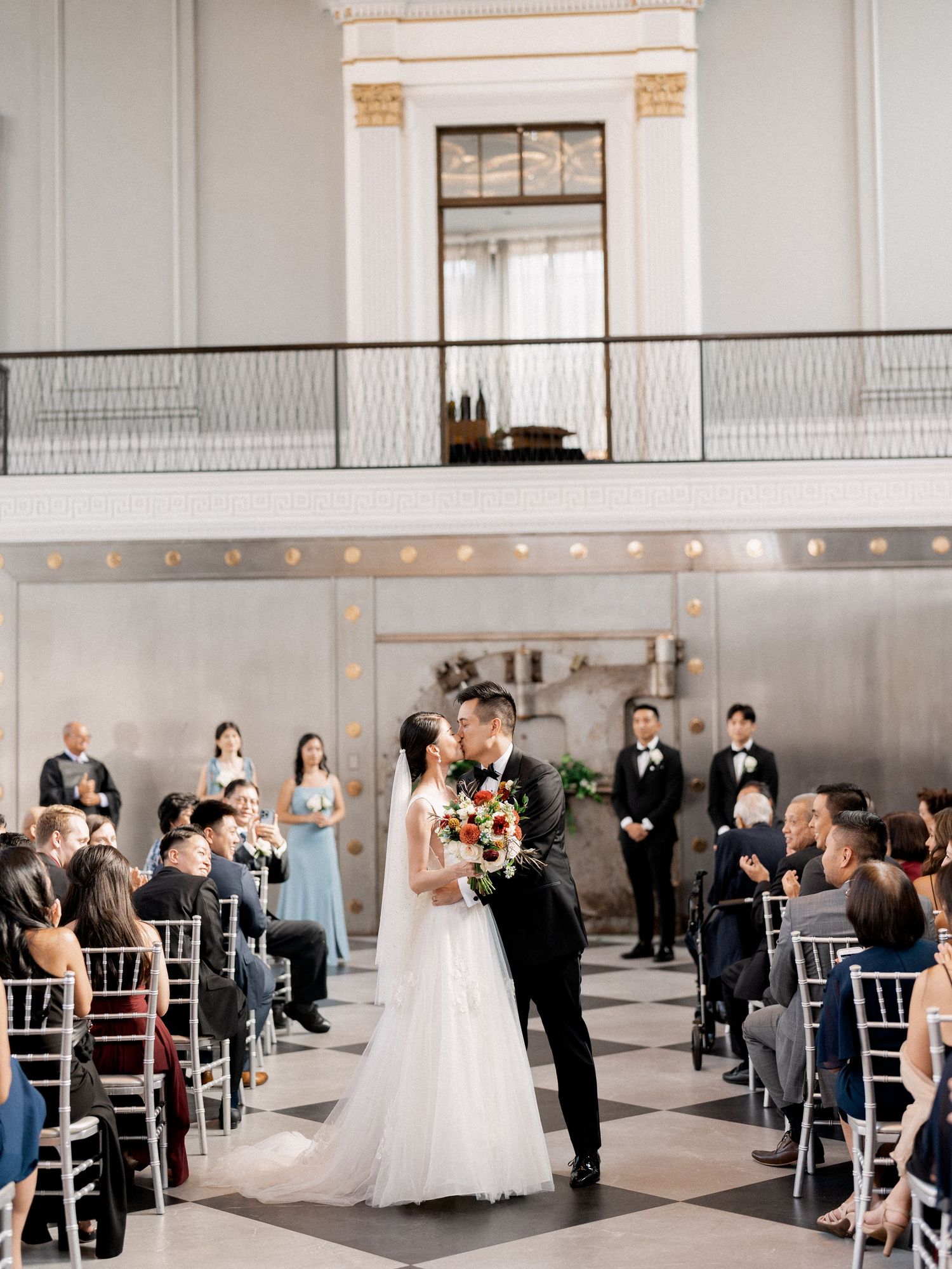 Wedding ceremony panorama in a bright modern venue with guests seated in rows.