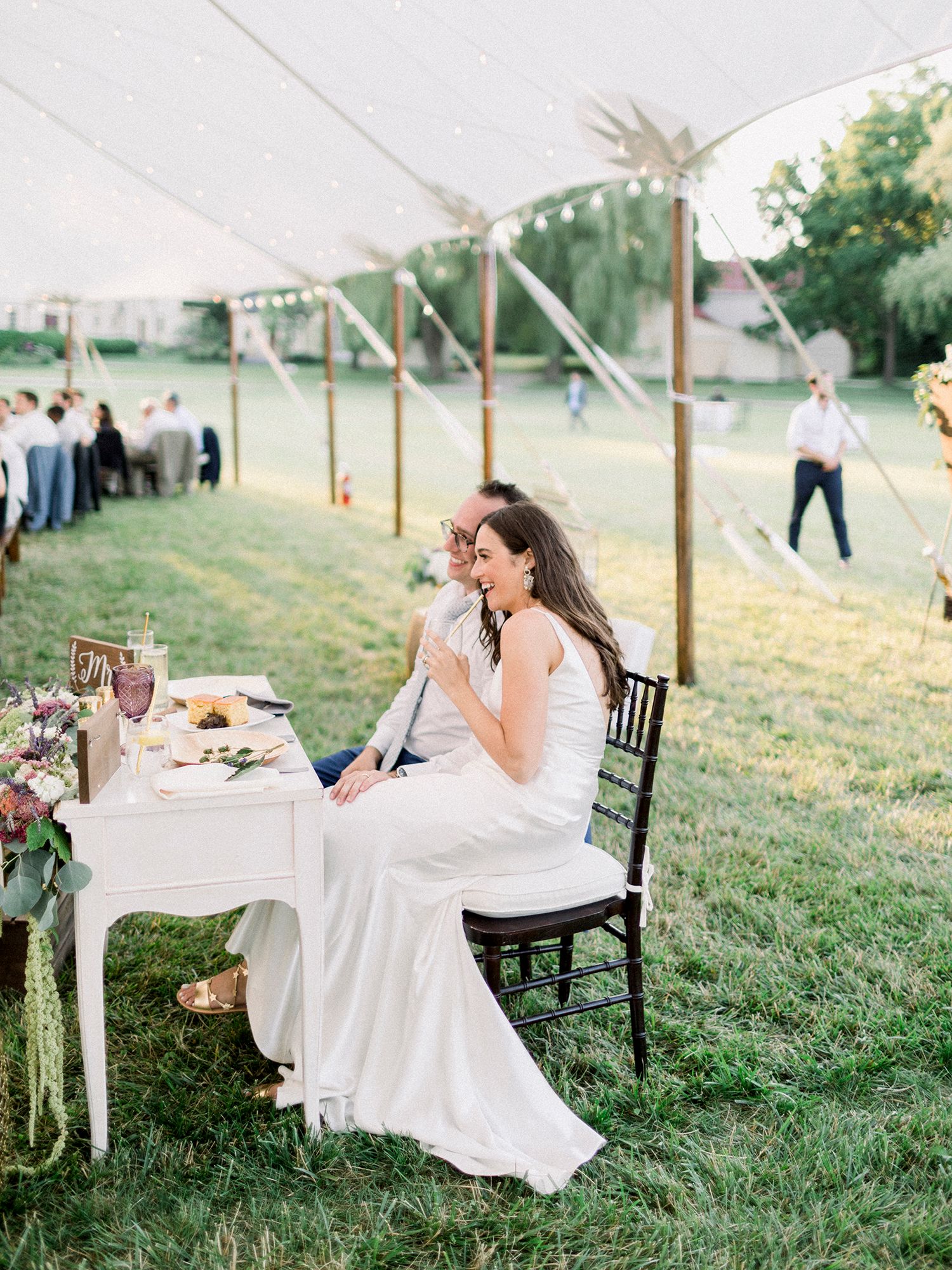 A person in a white dress sits at an elegantly set outdoor table during sunset.