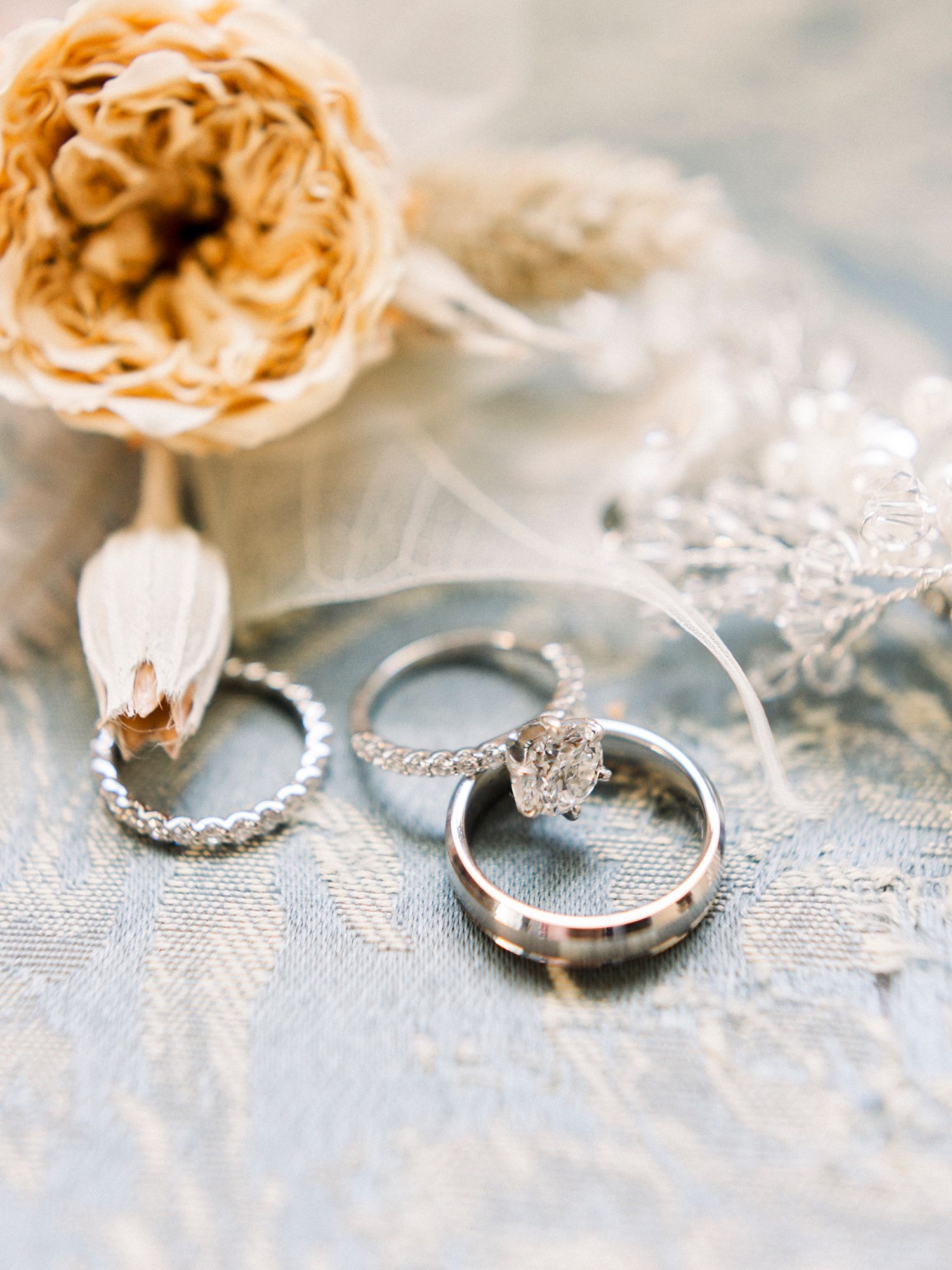 Wedding rings and jewelry displayed on delicate lace with soft natural lighting.