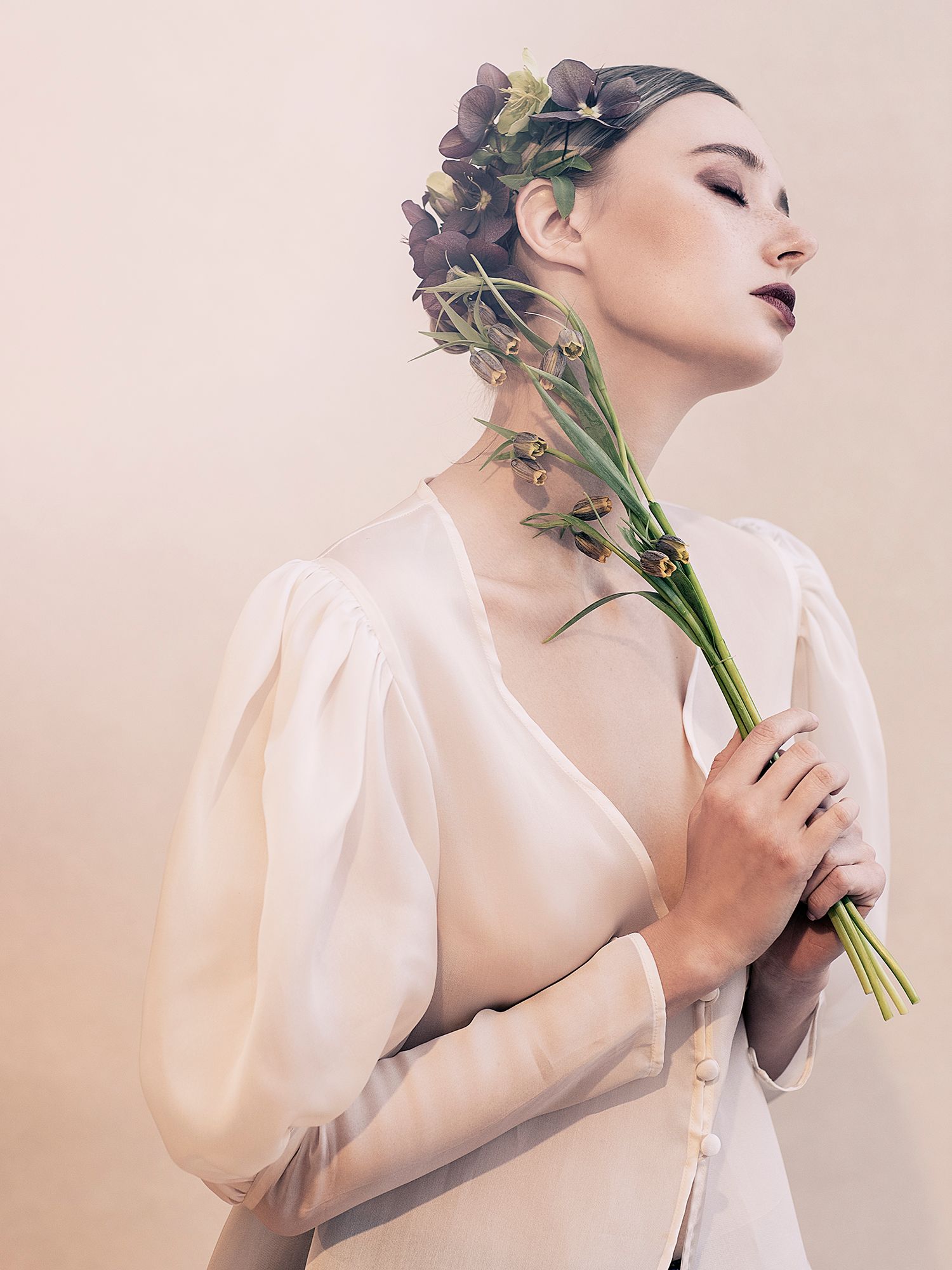 Artistic portrait in soft light featuring delicate flowers and sheer white fabric in a romantic ethereal style.