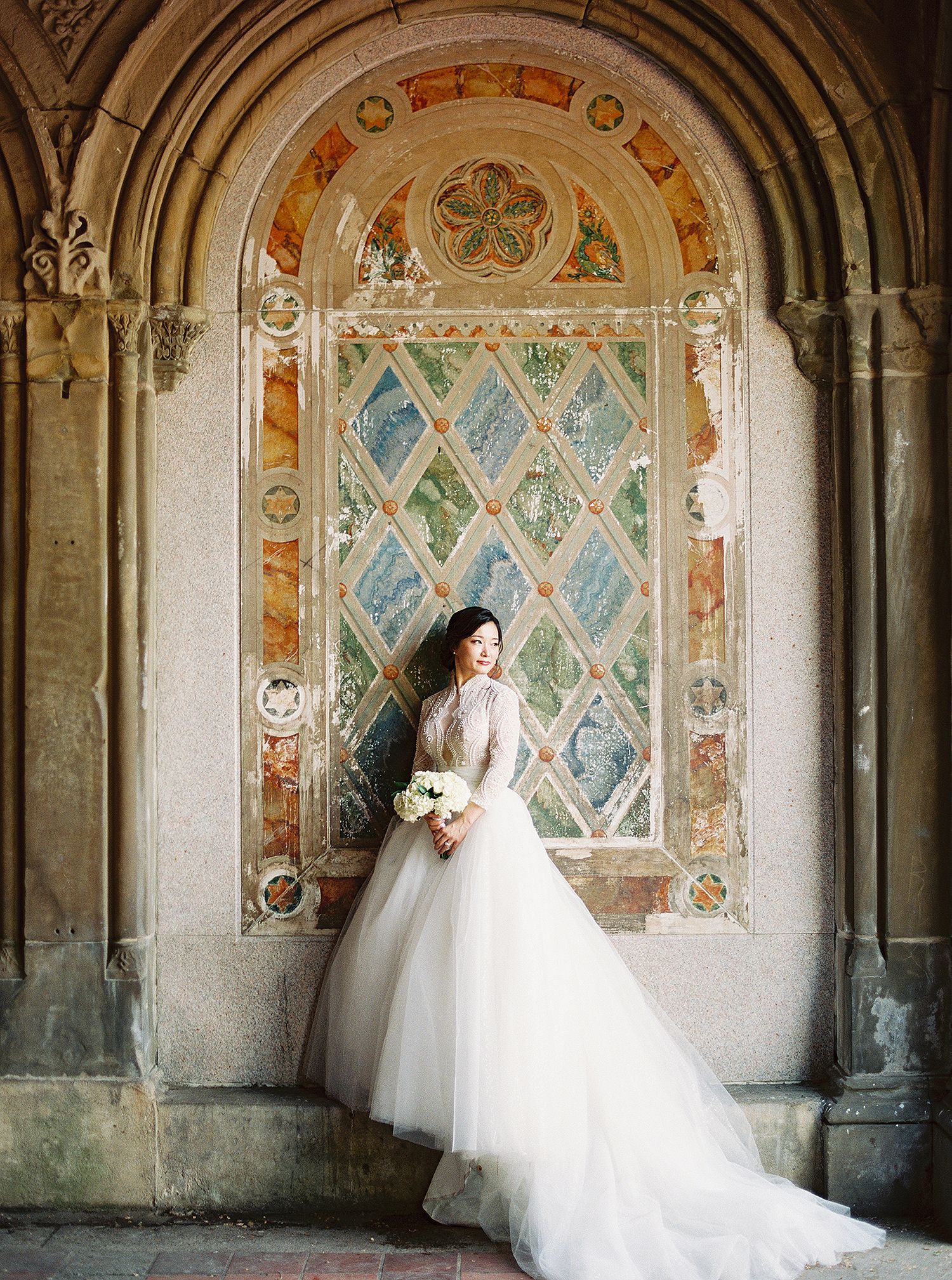 A wedding dress silhouette against ornate painted medieval wall murals in an ancient stone corridor. NYC wedding photographer.
