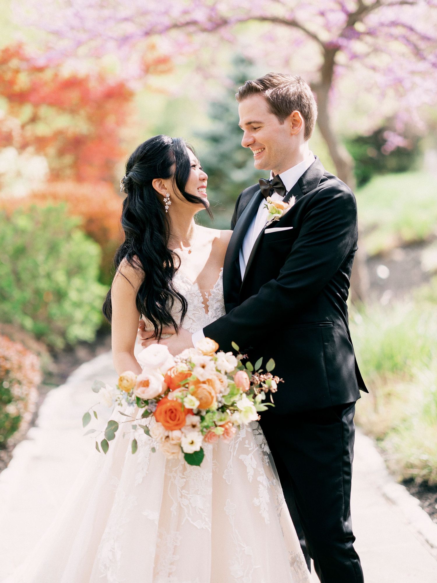 Romantic wedding portraits under pink cherry blossoms with coral and peach floral bouquet.