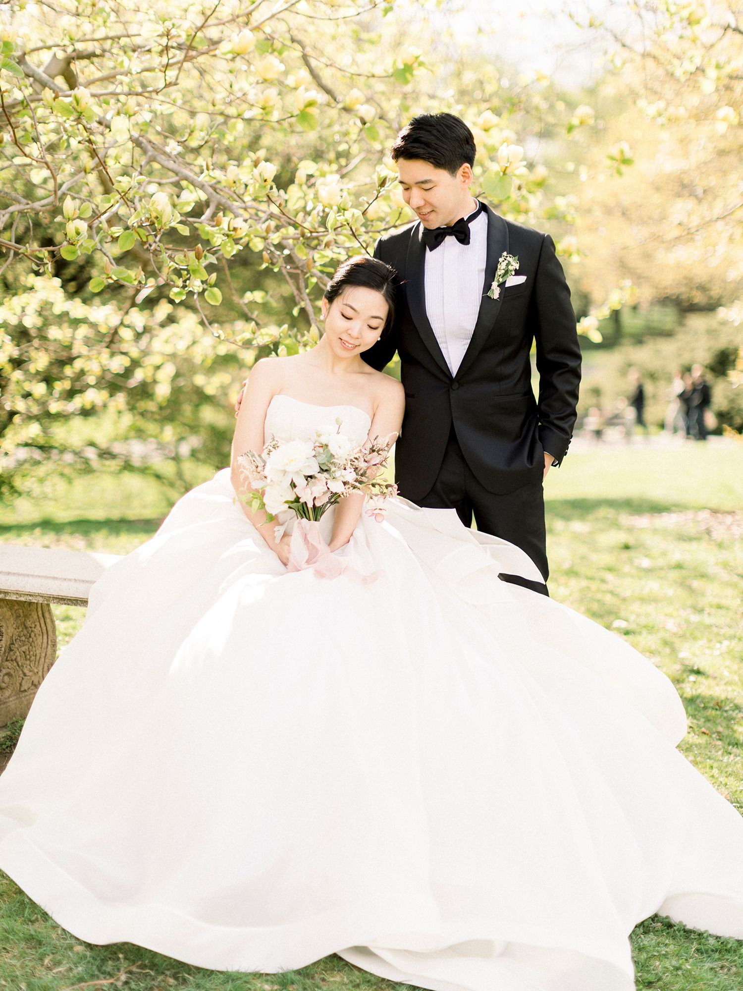 A romantic wedding photo shoot in a cherry blossom orchard with a flowing white gown and black tuxedo.