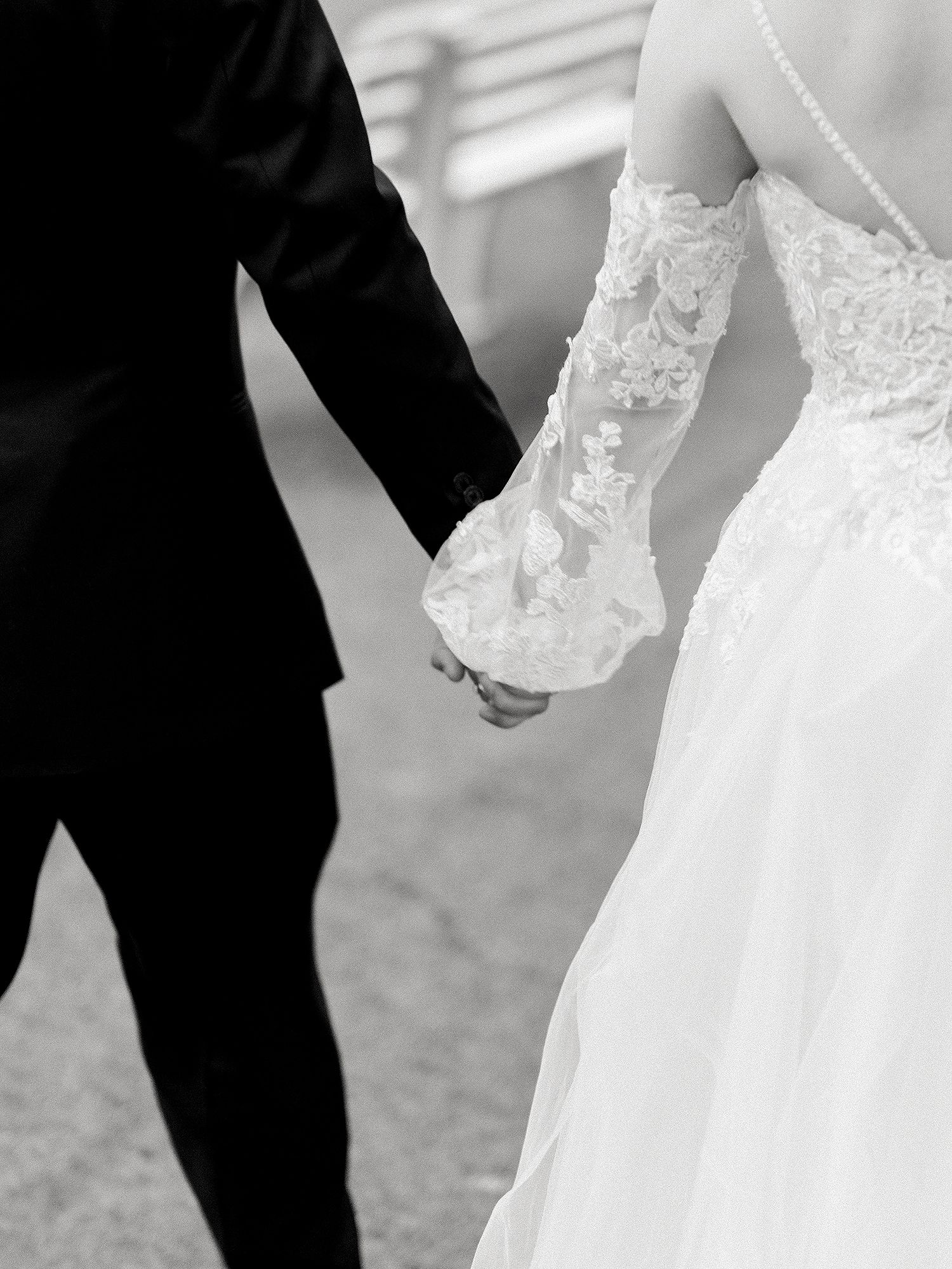 Close-up black and white photo of joined hands showcasing intricate lace wedding dress sleeve details. NYC wedding photographer.