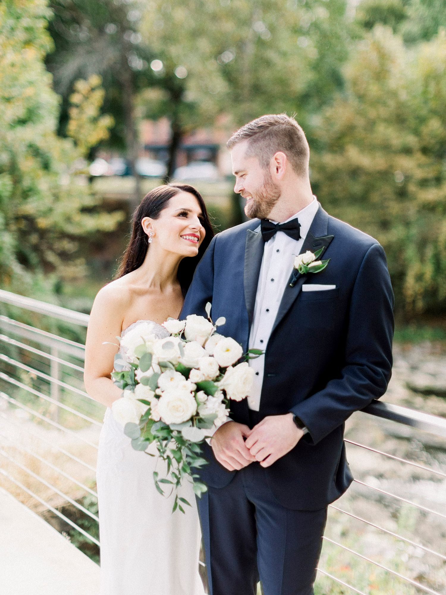 Wedding couple sharing intimate moments on outdoor path with white floral bouquet.
