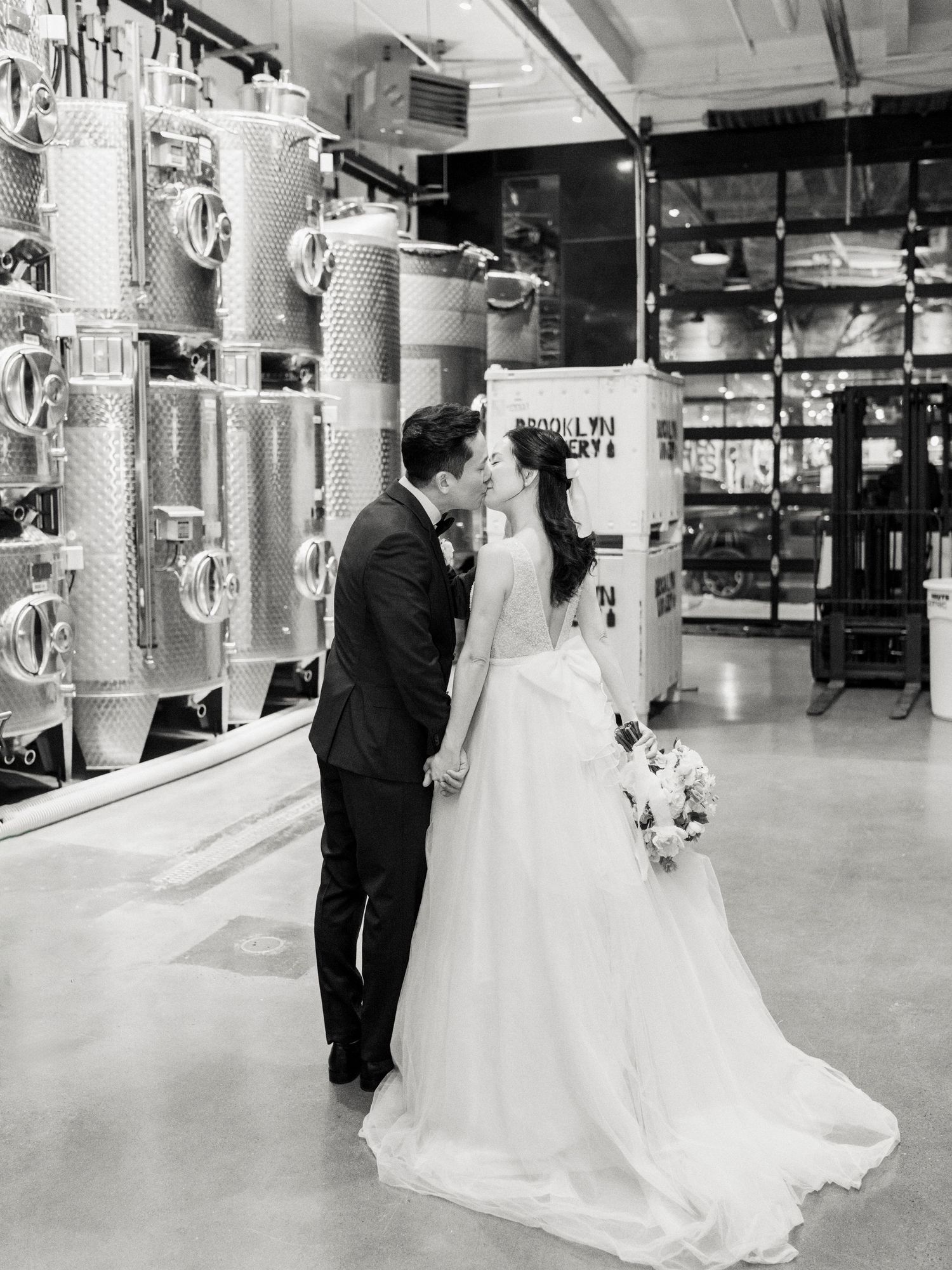 Black and white photo of a wedding couple in an industrial-style venue with metallic equipment.
