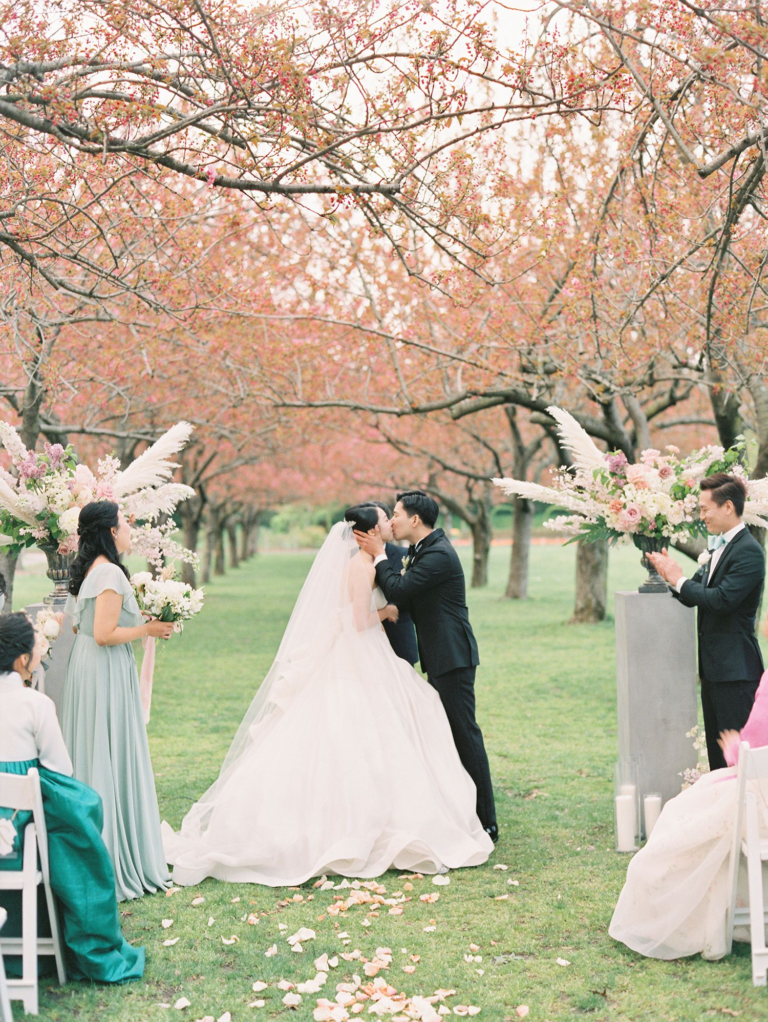 Wedding celebration with guests and decorative elements under pink cherry blossoms.