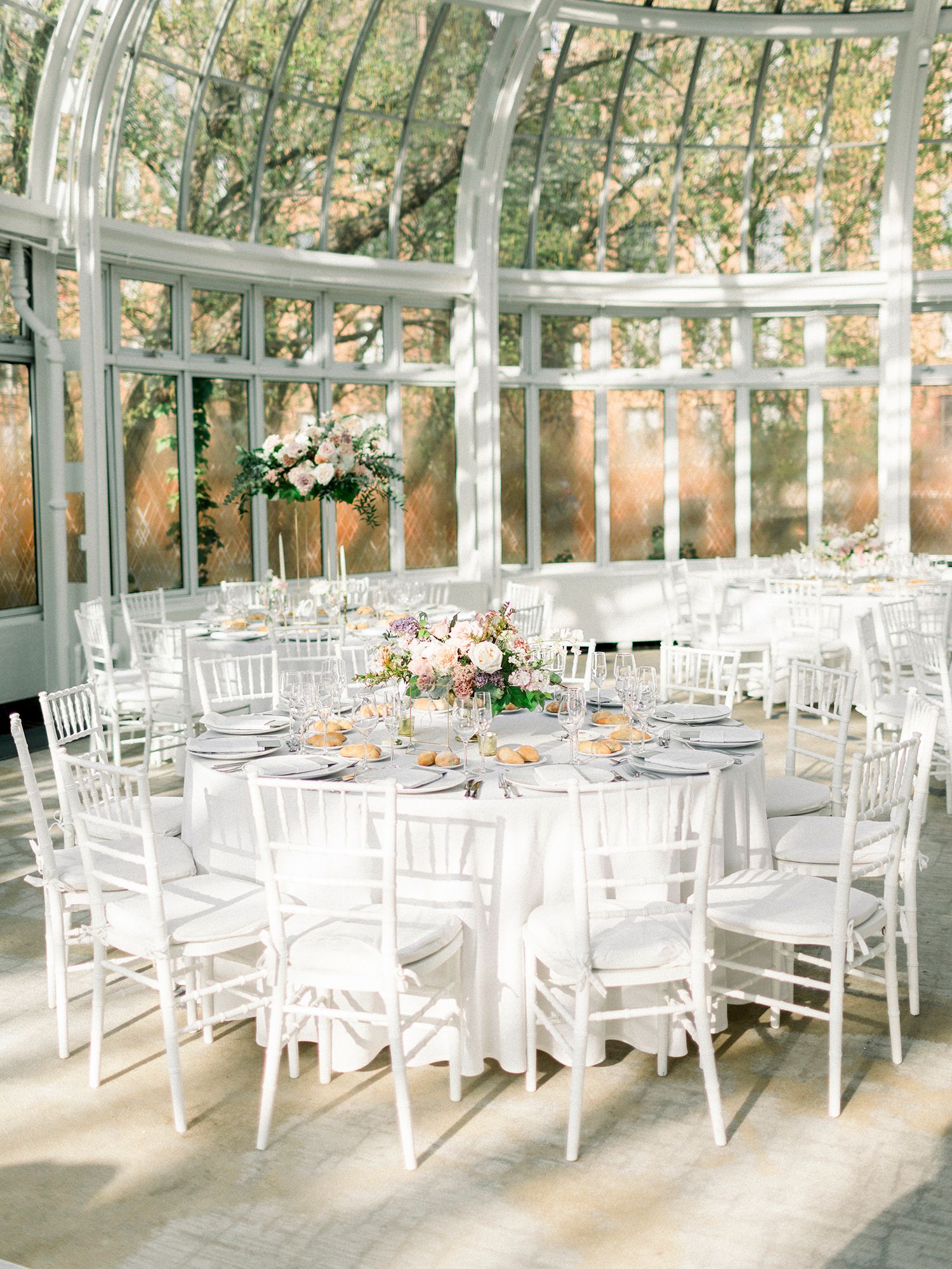 Elegant greenhouse wedding reception setup with white chairs and natural lighting.