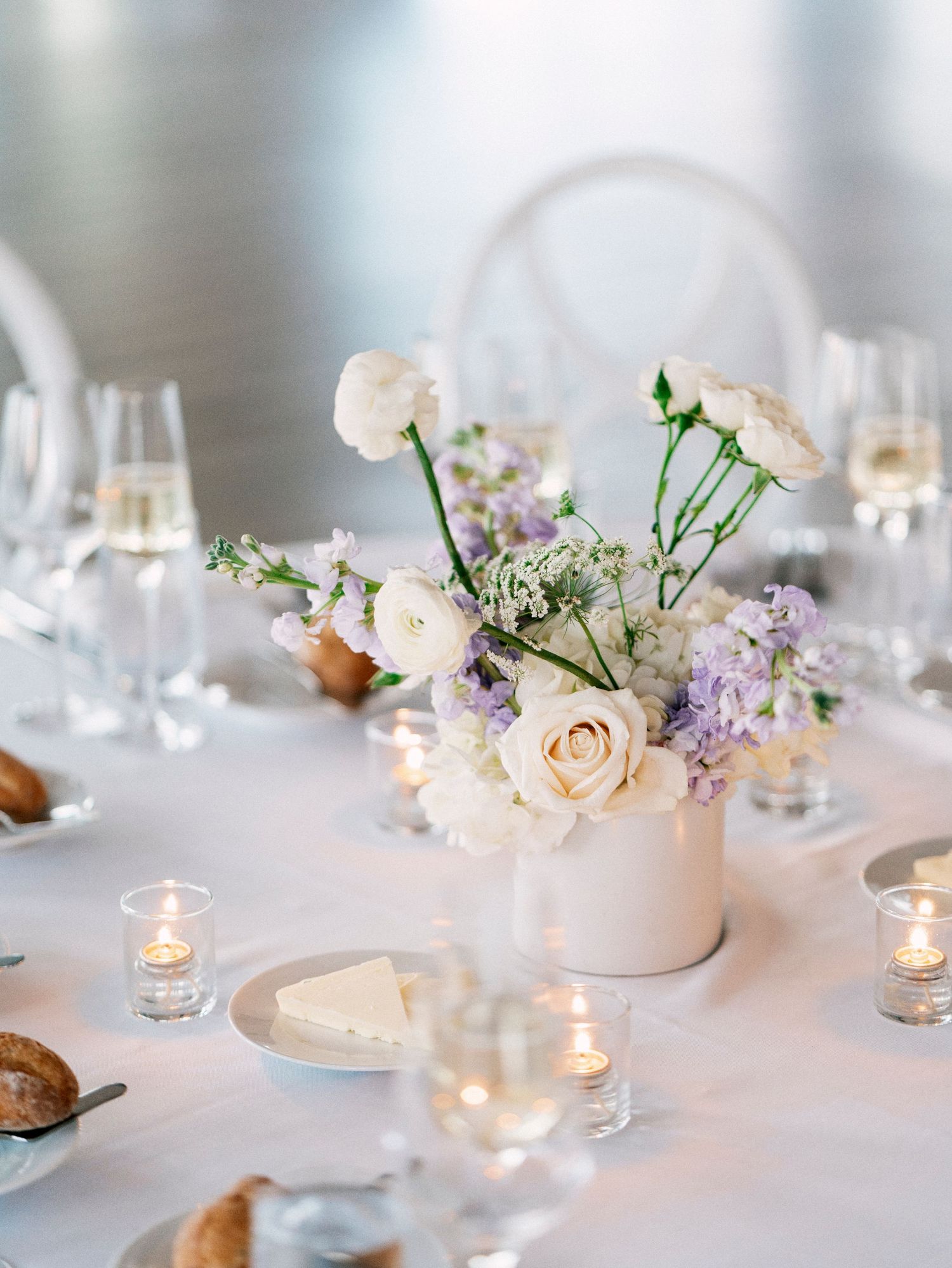 Elegant wedding table decor with soft pink roses and lilac flowers in white vases.