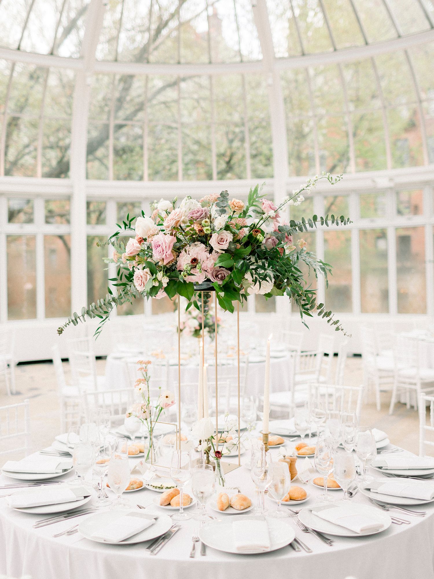 Light-filled conservatory wedding reception with elegant white table settings and floral centerpieces.
