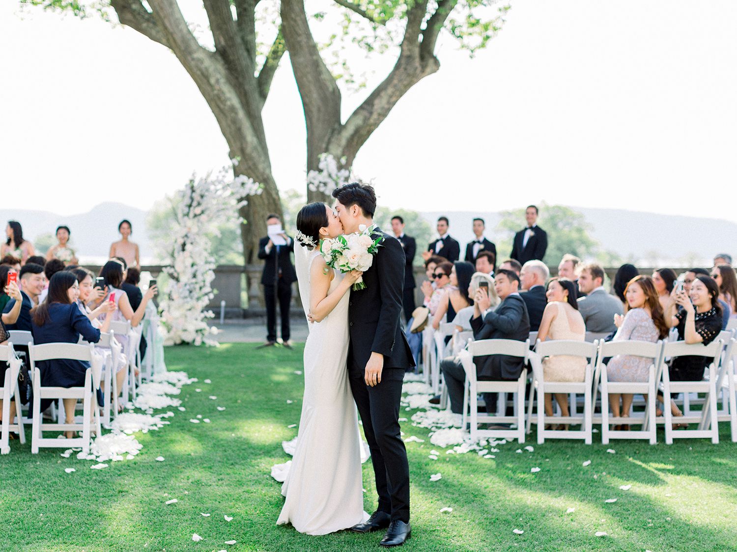 First dance moment at outdoor wedding reception with guests seated in white chairs under tree canopy. NYC wedding photographer.