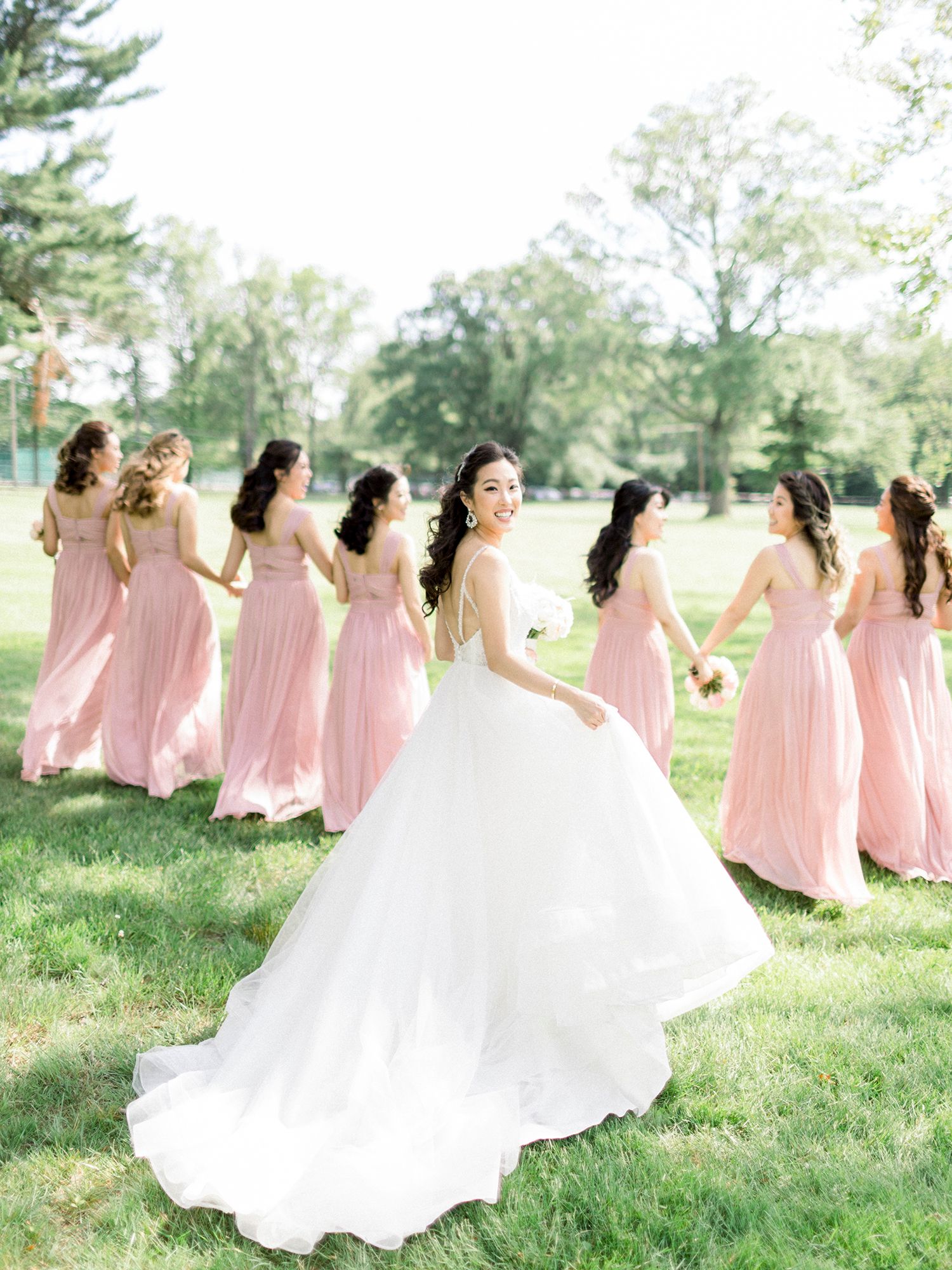 Bridesmaids in pink dresses posed on grassy lawn with bride in white gown.