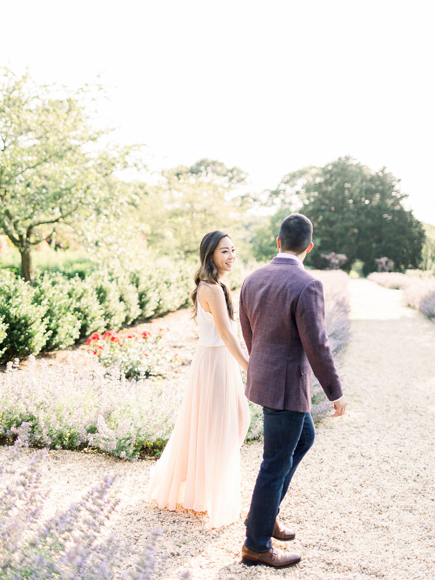 A couple strolling through a blooming garden path in formal attire.