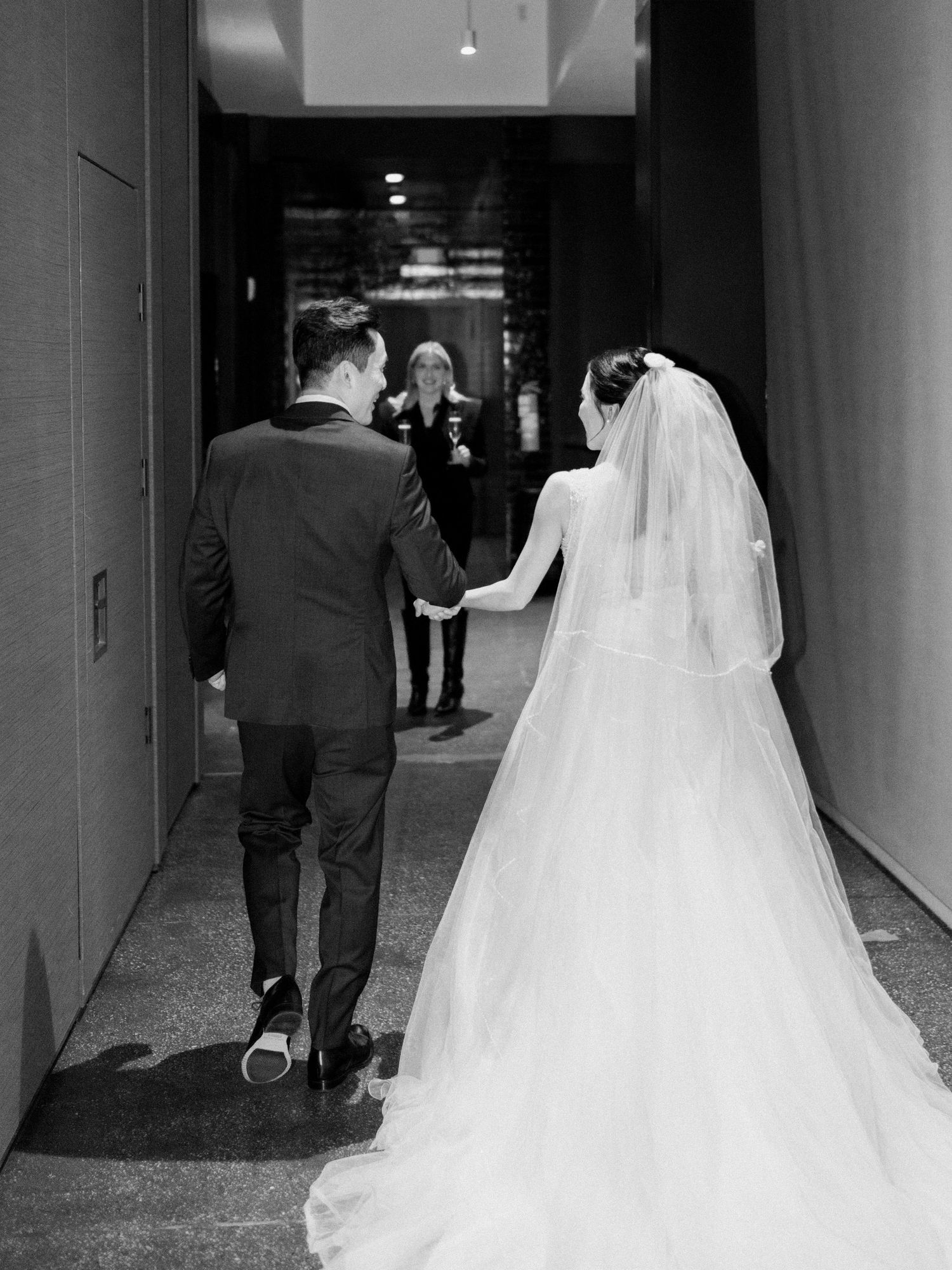 Wedding party walking through a modern hallway with dramatic lighting and shadows.