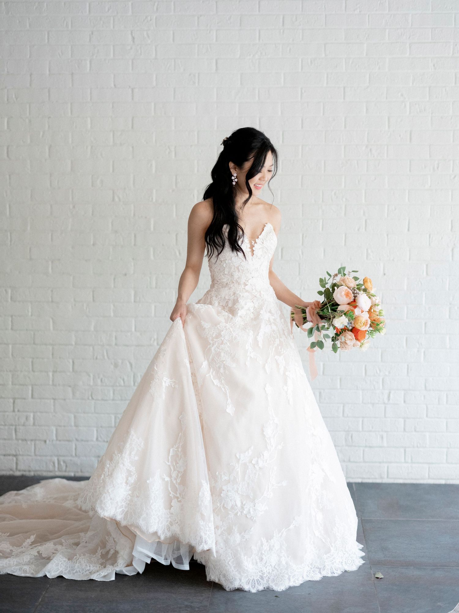 Bridal portraits against white brick wall showcasing lace wedding dress details.