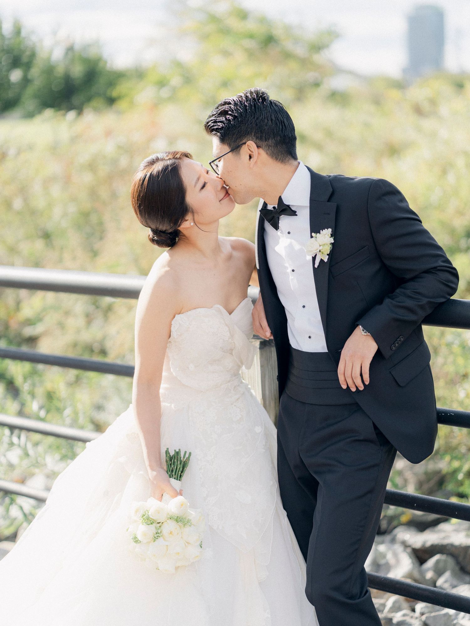 Romantic wedding couple shares intimate moments along a waterfront railing with city views.