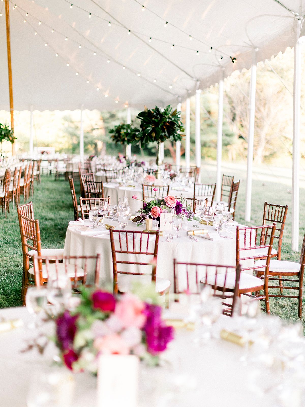 Elegant outdoor wedding reception under white tent with pink floral centerpieces and chiavari chairs.