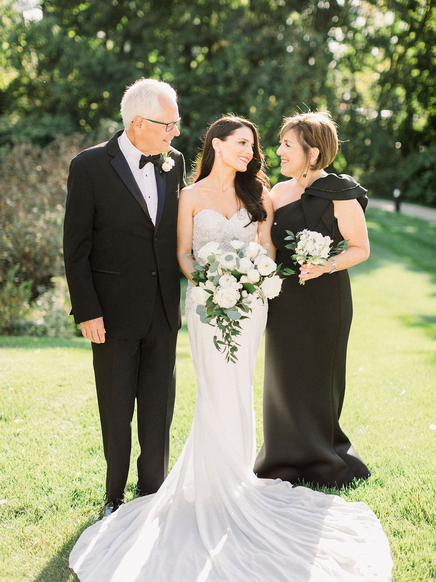 Wedding party members in formal attire gather for outdoor garden portraits.