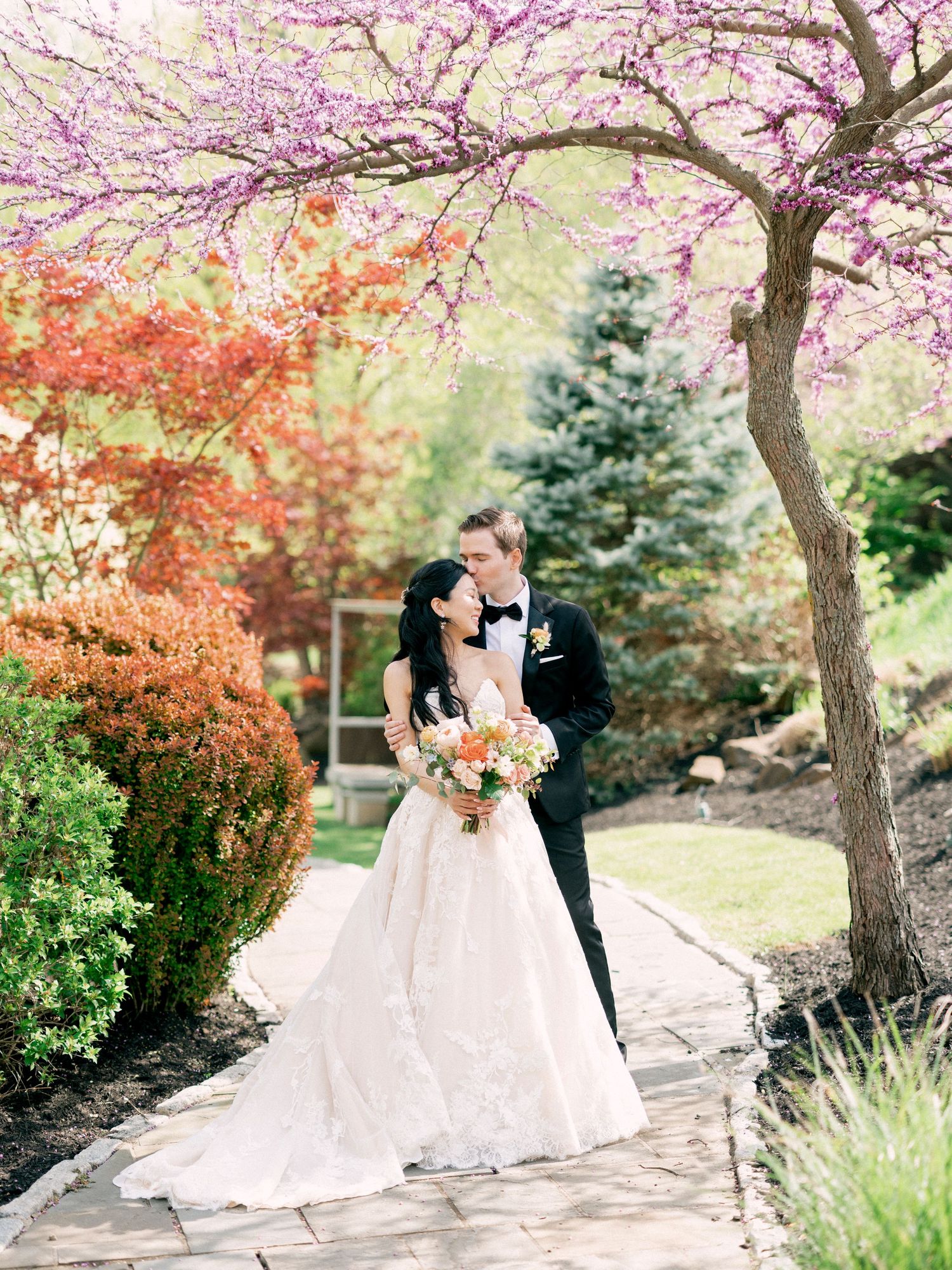 Wedding portraits captured under blooming cherry trees on a garden path.