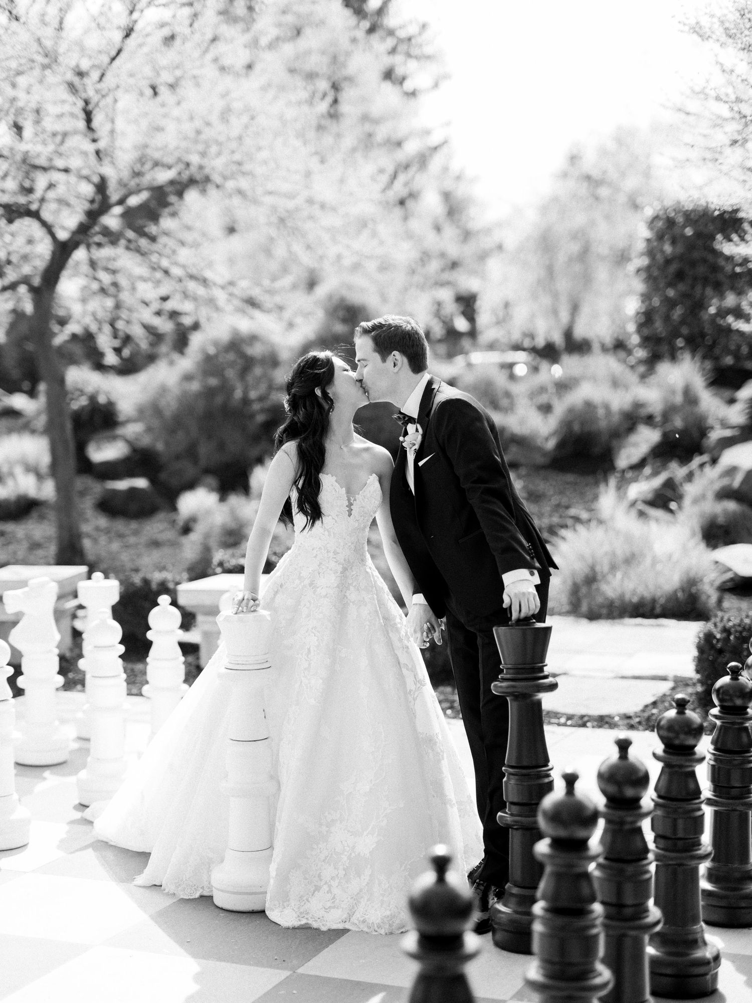 Artistic black and white wedding photos with giant chess pieces in an outdoor setting.