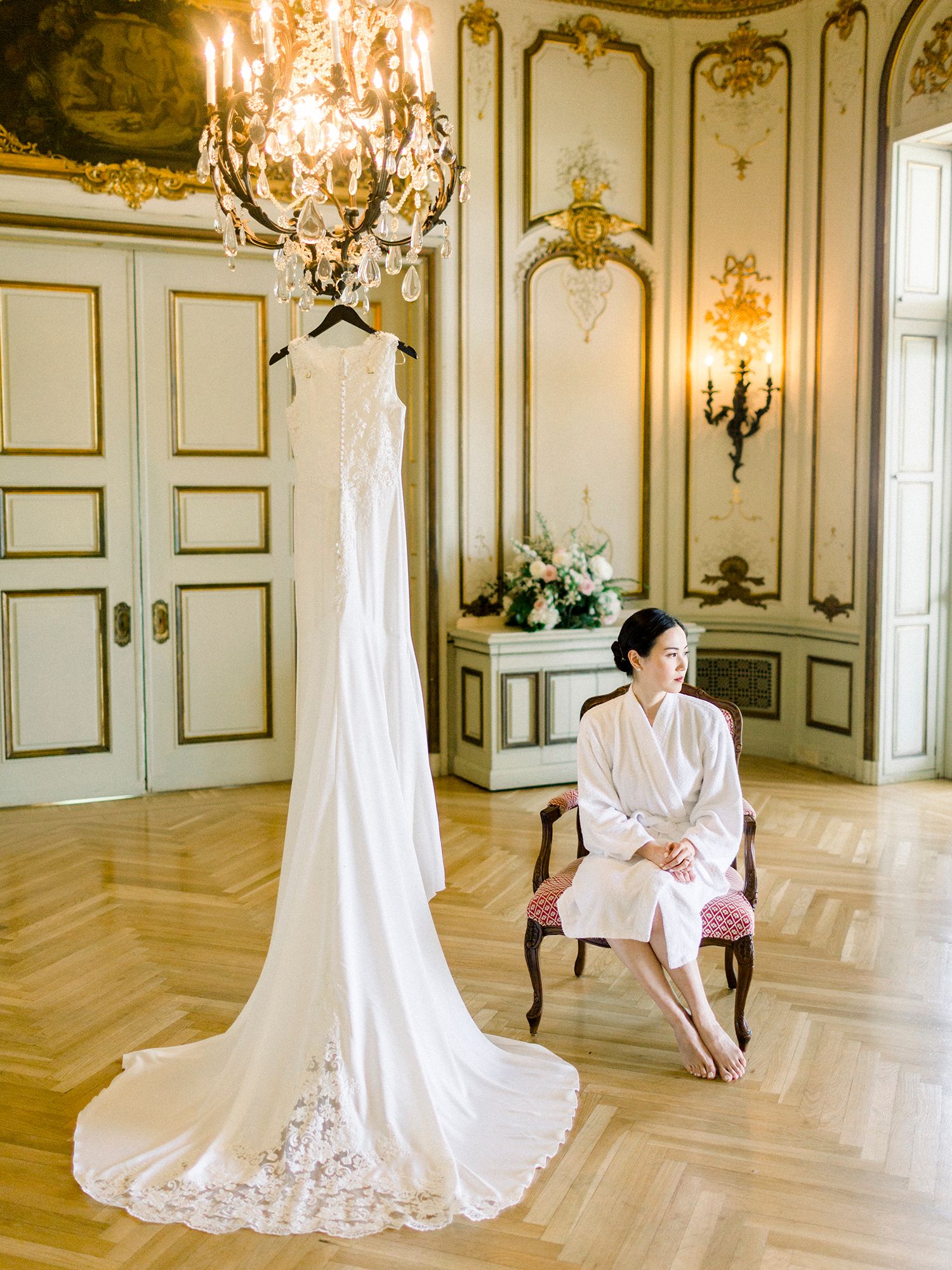 Ornate ballroom with gold trim, crystal chandeliers and a flowing white wedding dress on display.