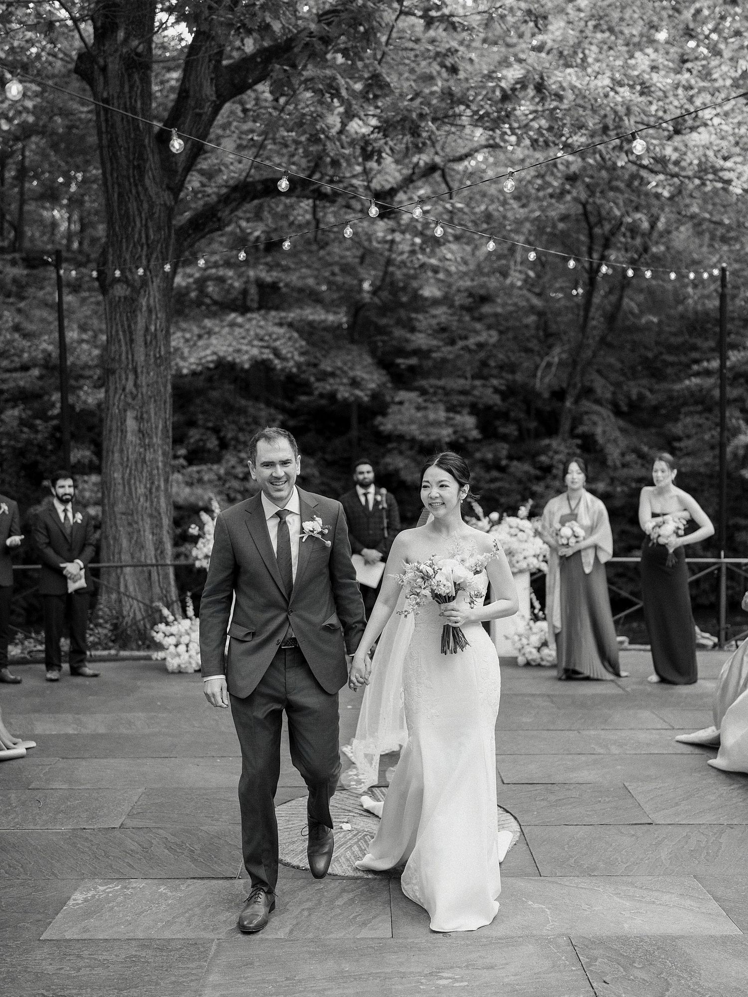 Wedding party celebrating on stone patio surrounded by trees in black and white.