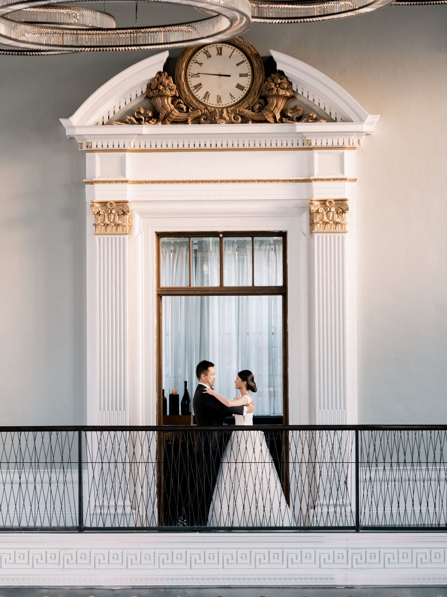 Architectural wedding photos with couple on balcony under ornate clock and columns.
