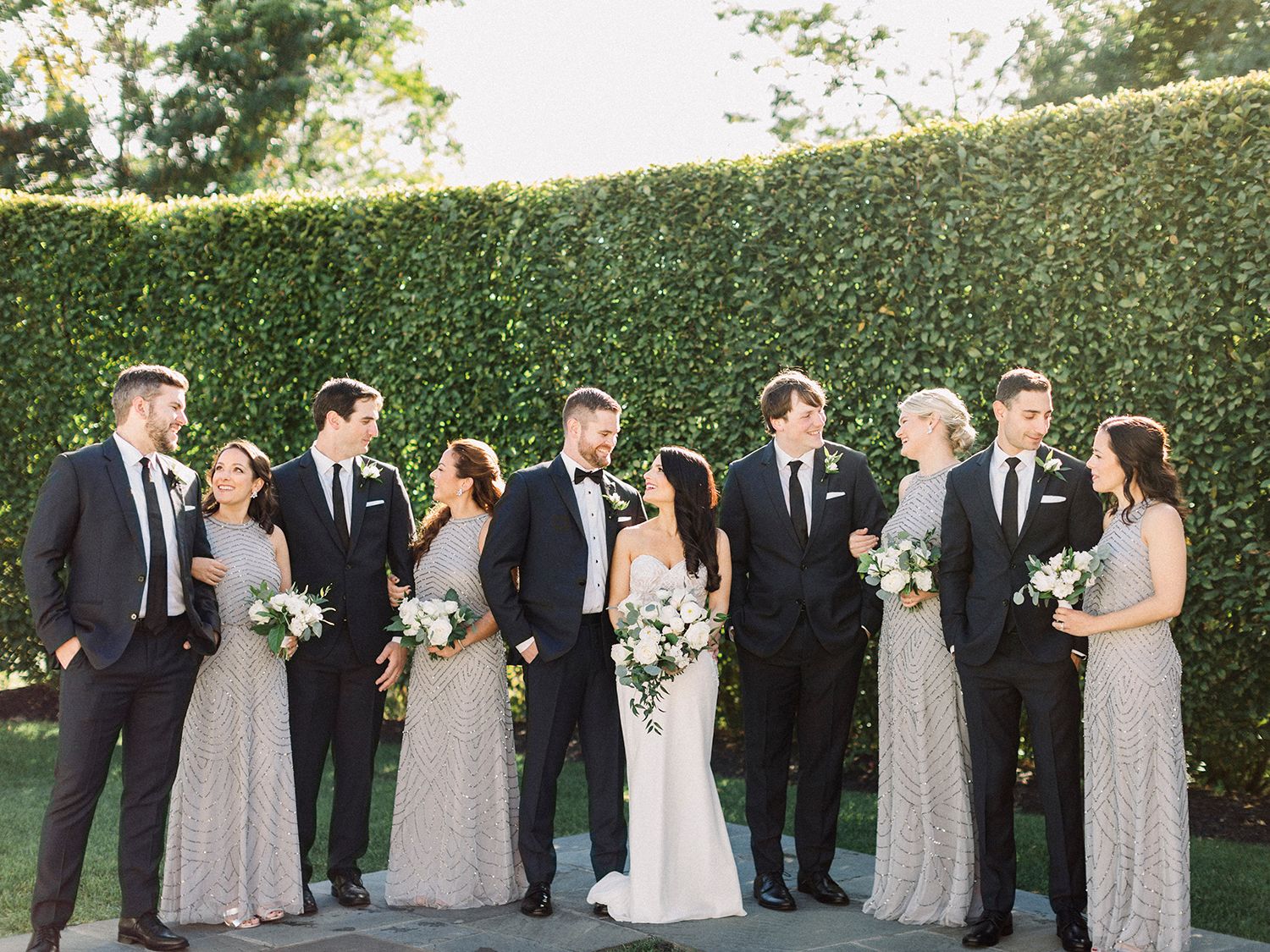 Full wedding party portrait with bridesmaids in silver and groomsmen in black suits.