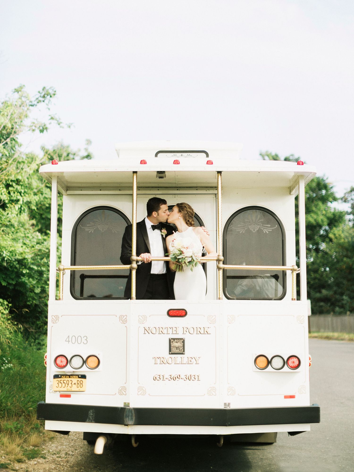 Newlyweds share an intimate moment in the back window of a vintage white shuttle bus.