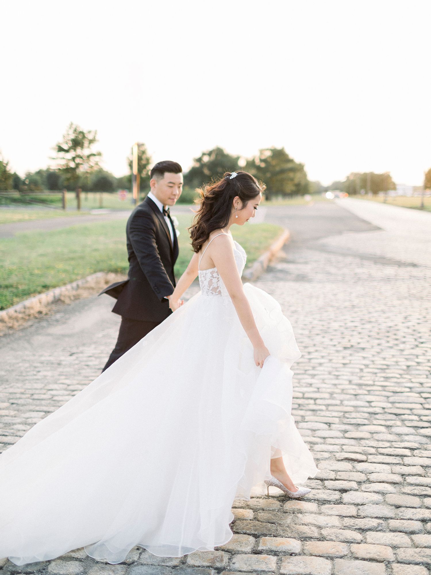 Couple walking together on cobblestone path in formal wedding attire.