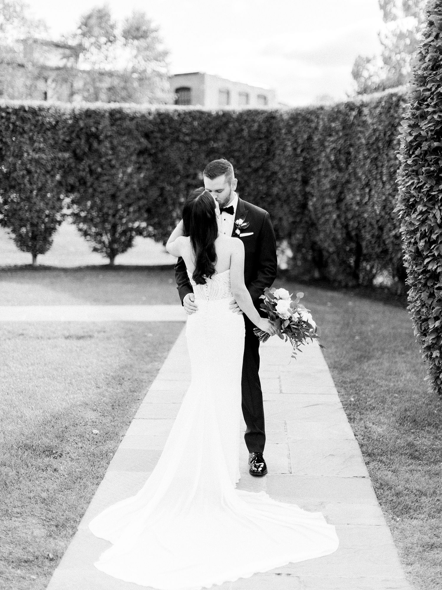 Romantic black and white wedding portraits of a couple in formal attire walking along a garden path.