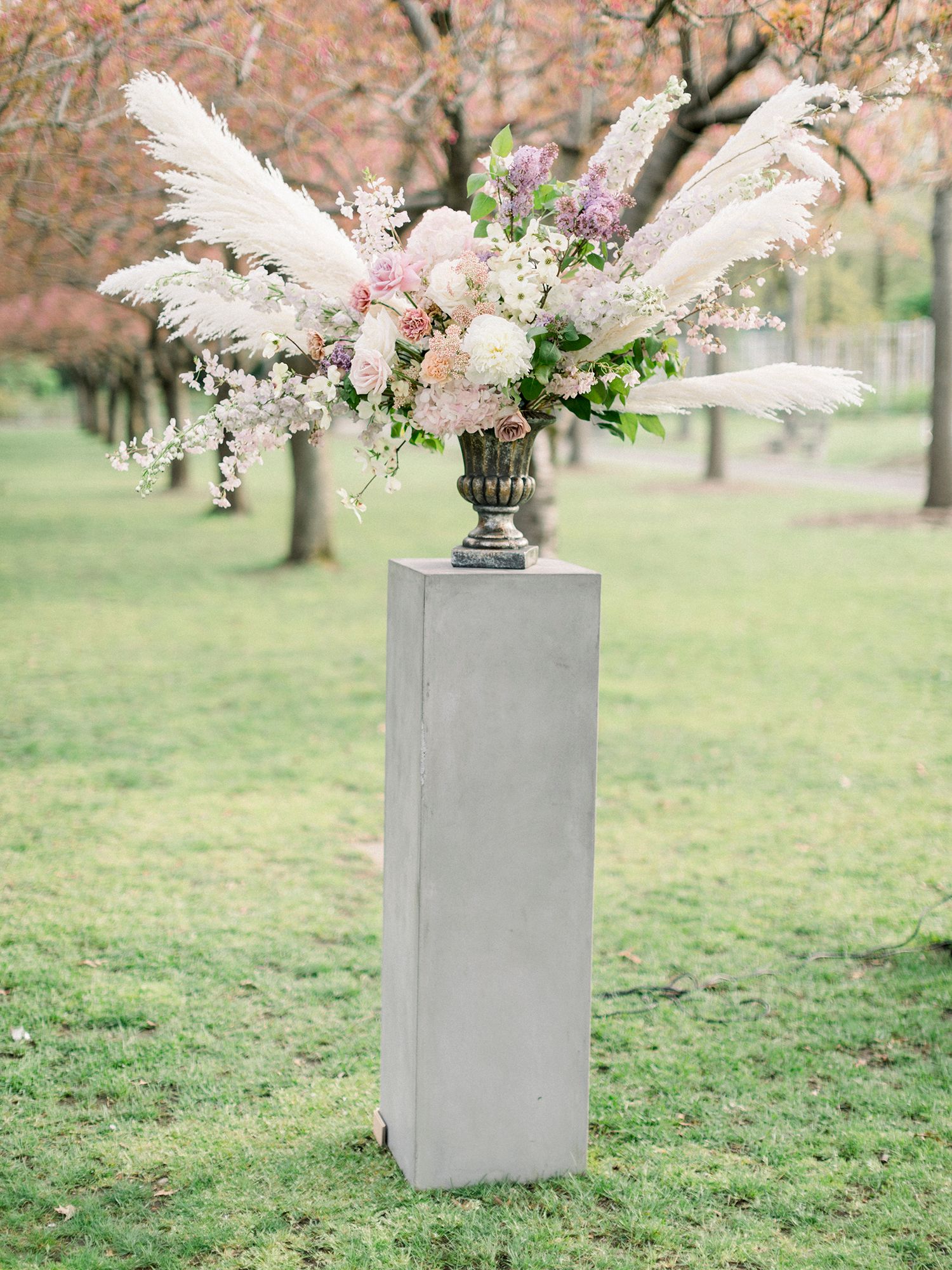 Modern white floral arrangements displayed on gray pedestals beneath cherry blossom trees.