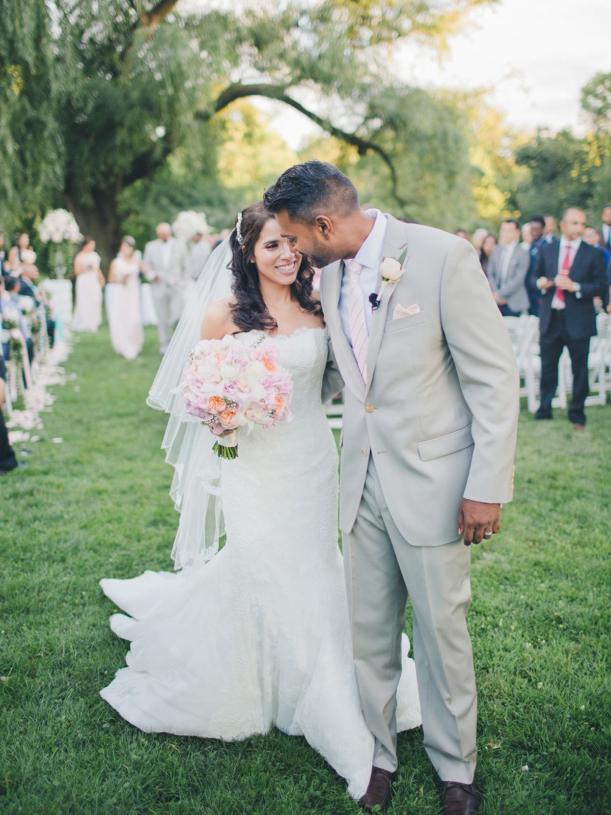 A tender wedding moment captured outdoors with guests looking on in the background. NYC wedding photographer.