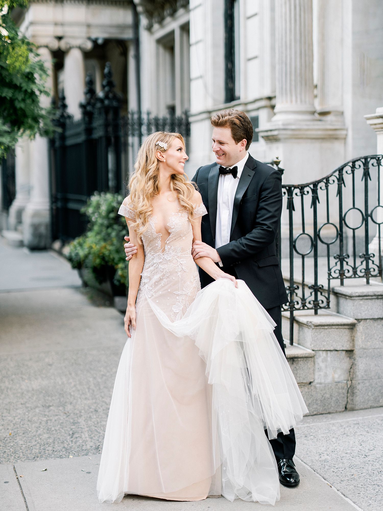 A romantic wedding couple dances and twirls on a cobblestone path beside ornate columns. NYC wedding photographer.