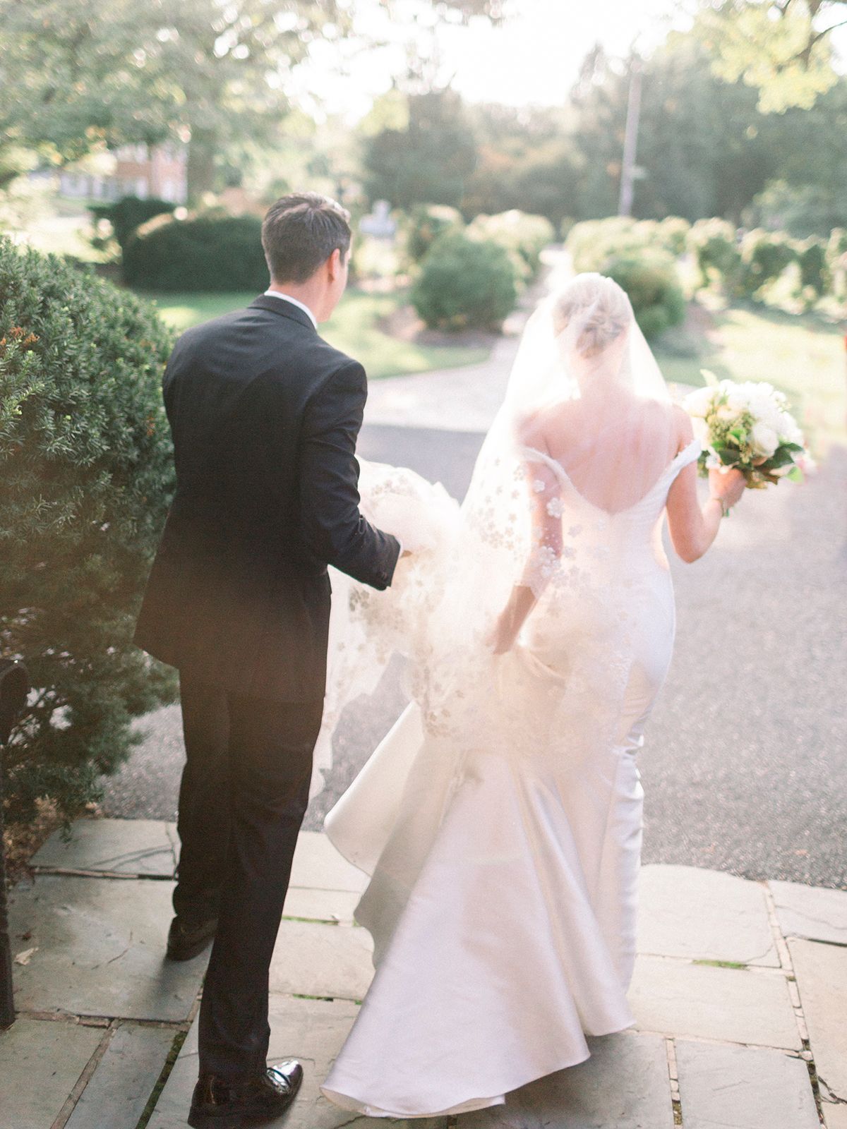 Romantic couple walking along a garden path in formal wedding attire.