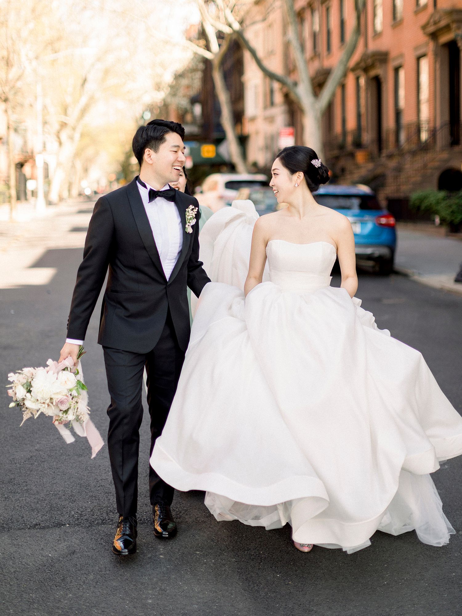 Newlyweds walk together on city street with bride's dress flowing behind them. NYC wedding photographer.