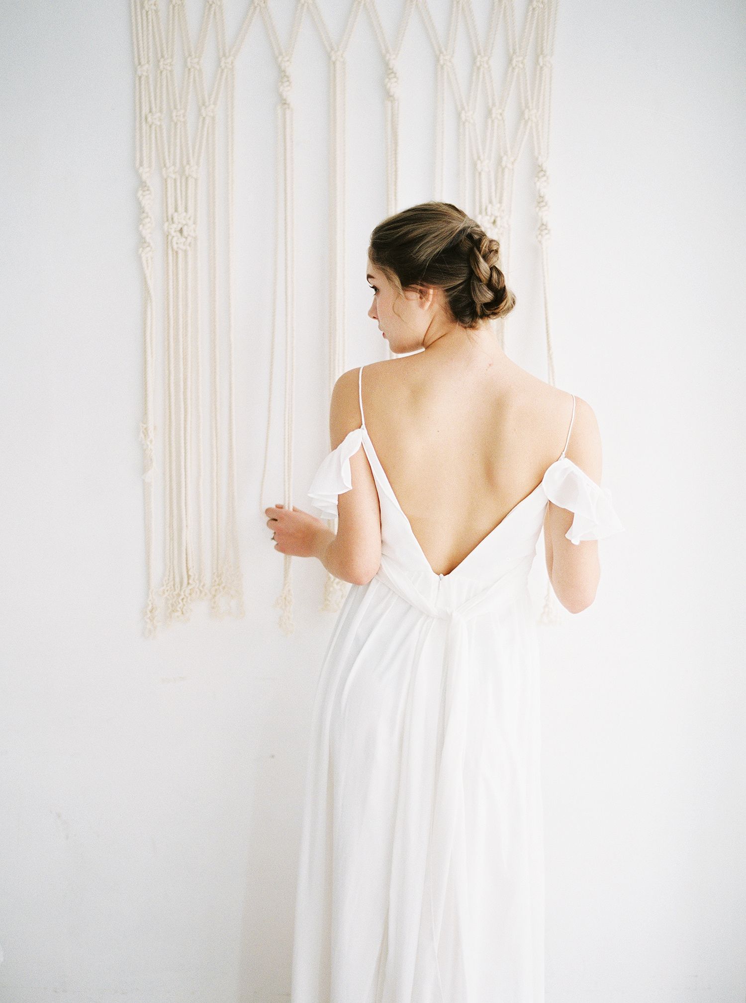 Minimalist white dress photographed against macrame wall hanging in soft natural light.
