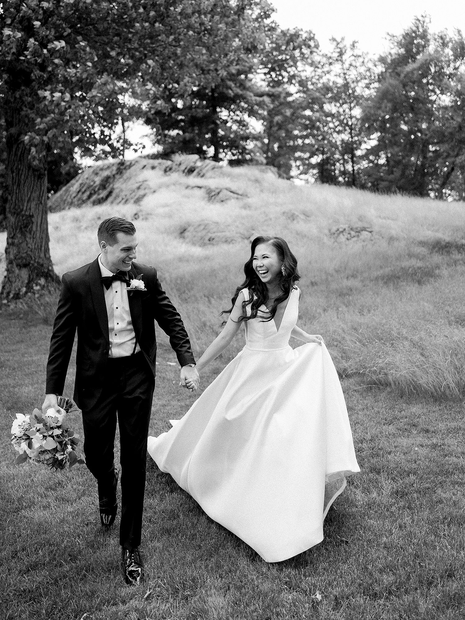 Black and white wedding photos of a couple playfully running through a grassy hillside. NYC wedding photographer.