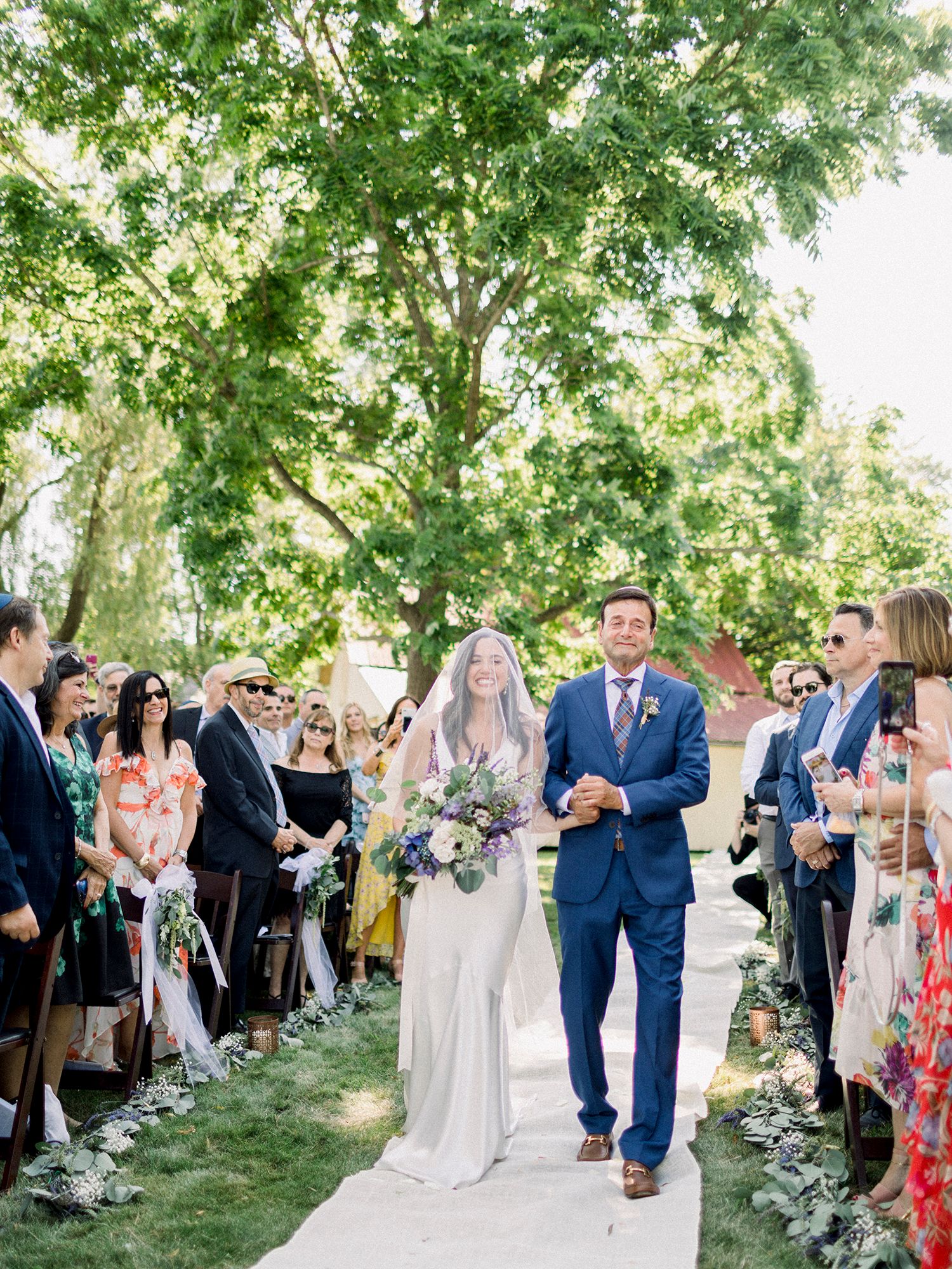 Couple walks down white aisle runner during outdoor garden wedding ceremony.