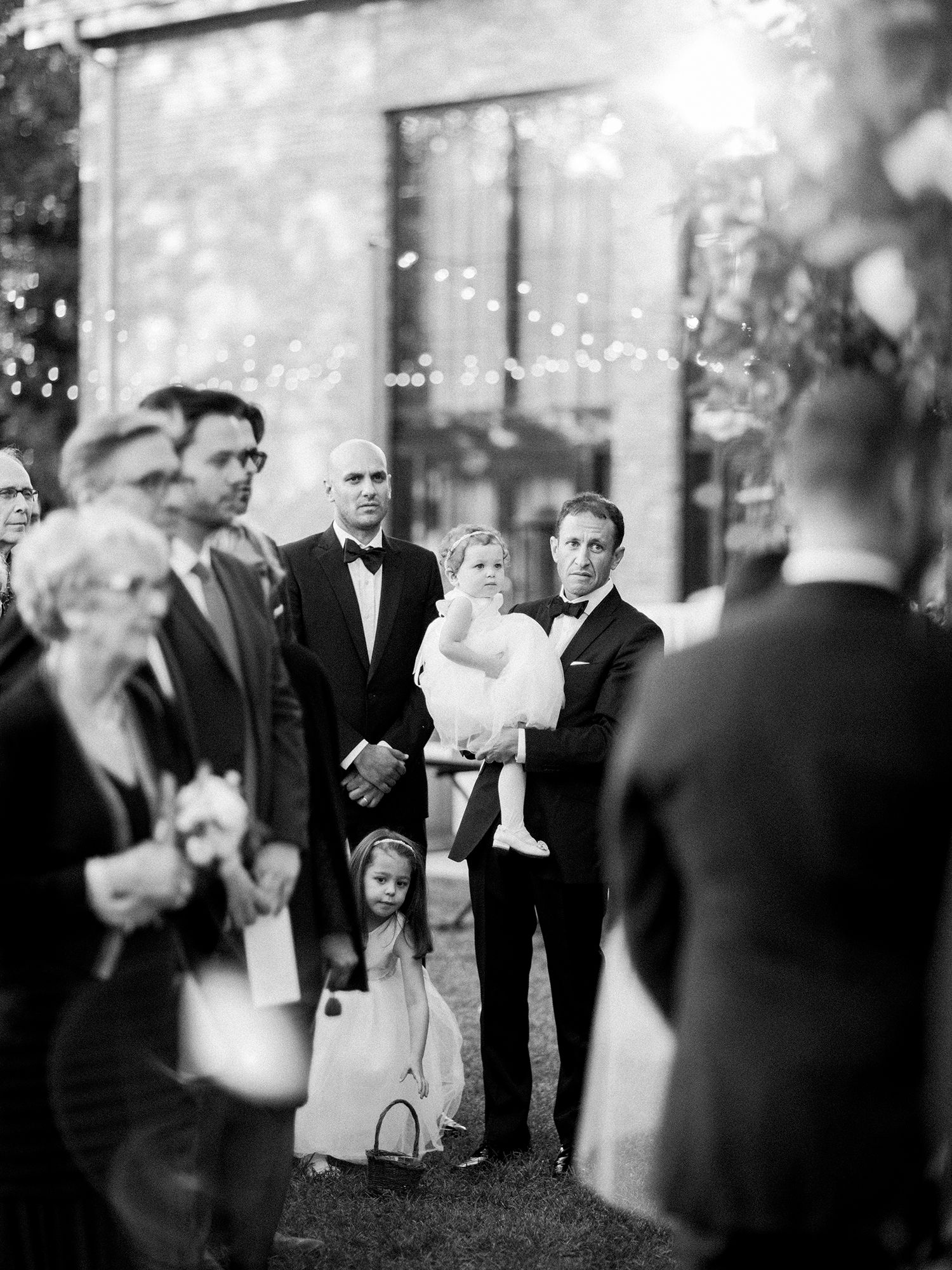 Wedding guests in formal black tie attire socializing during an outdoor evening reception.