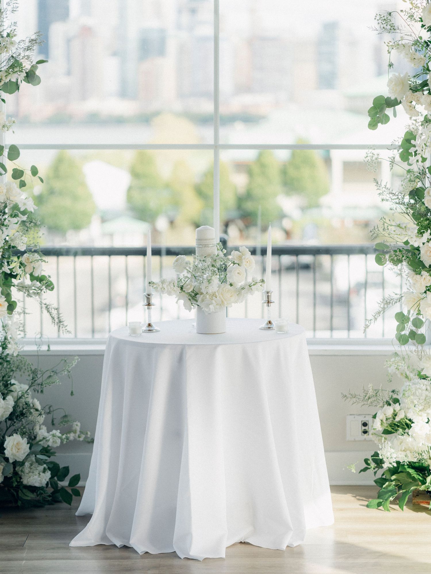 Elegant wedding reception setup with white tablecloths and floral arrangements against city views.