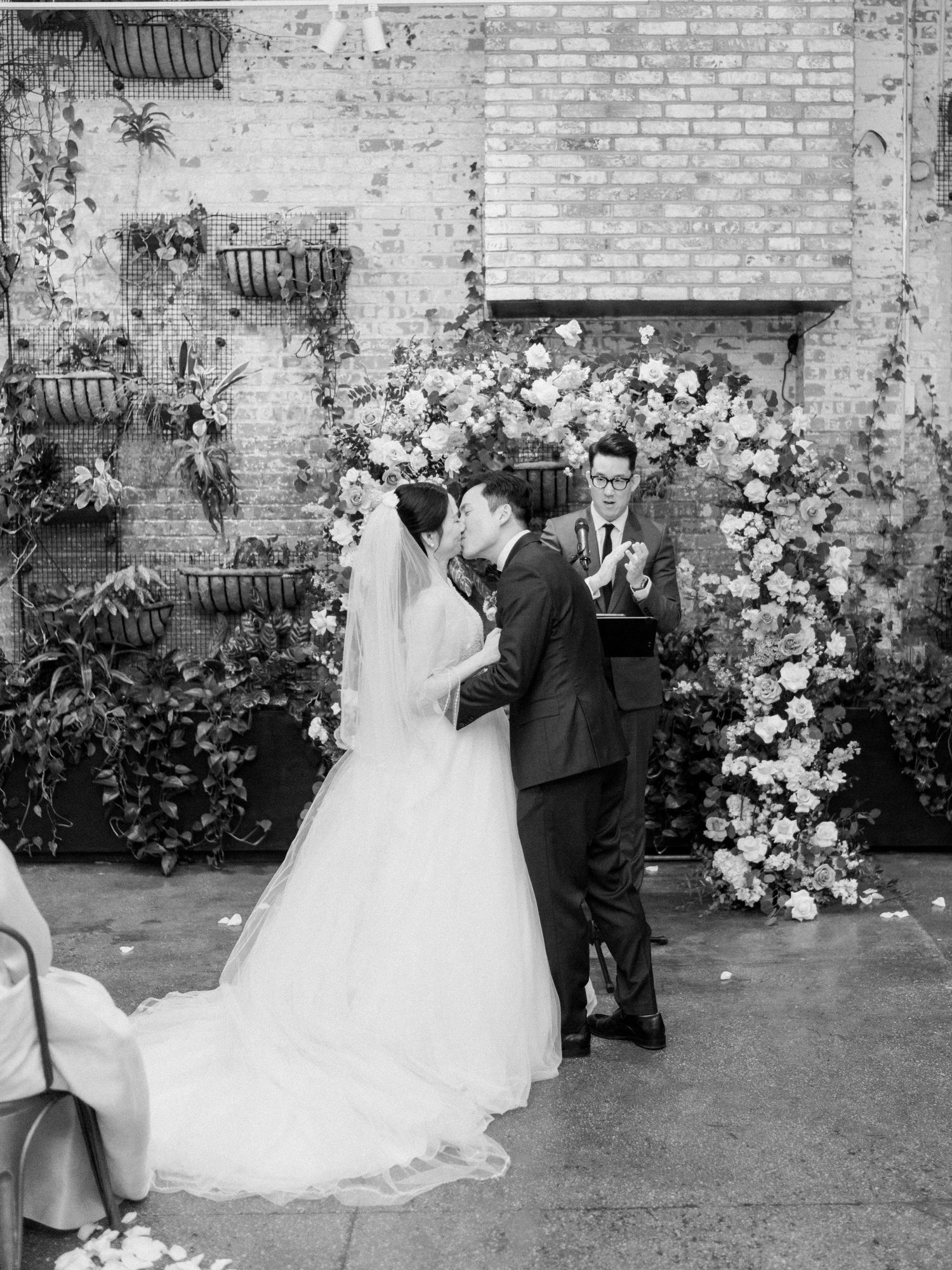 Romantic wedding scene against a brick wall with lush white floral decorations.