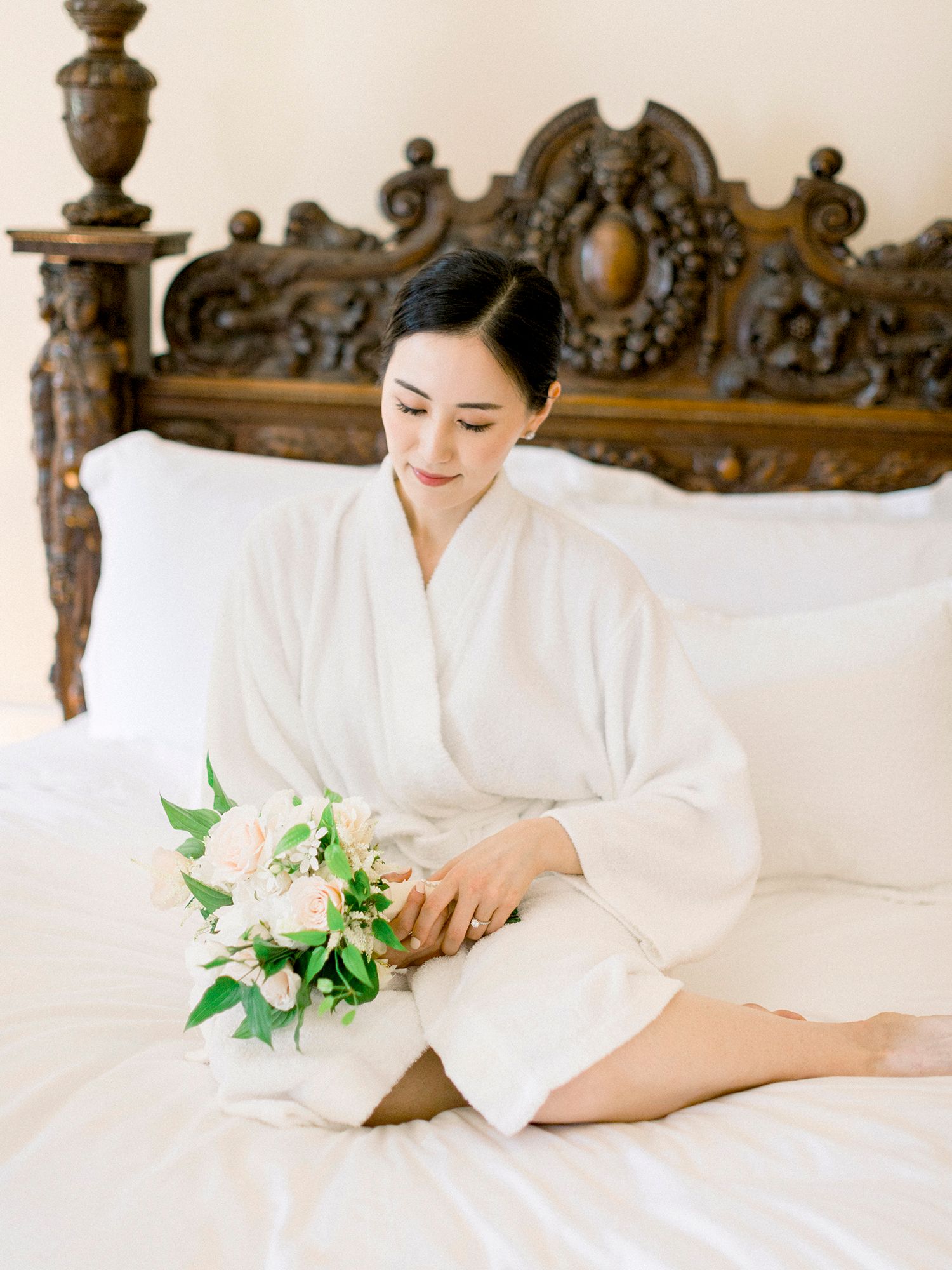 Bridal preparation scene on an ornate bed with white linens and green floral accents.