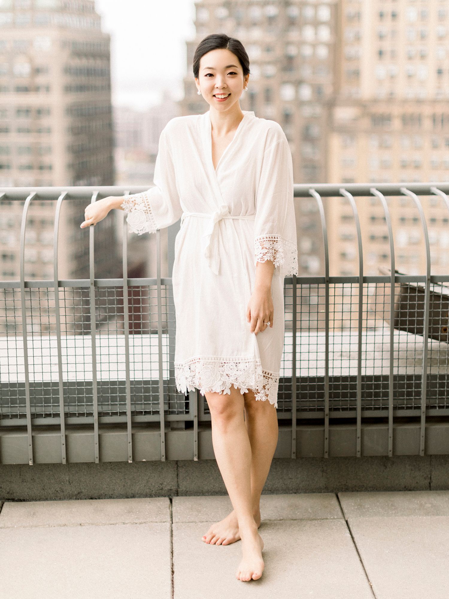 Person in white dress poses on urban rooftop with city buildings in background.