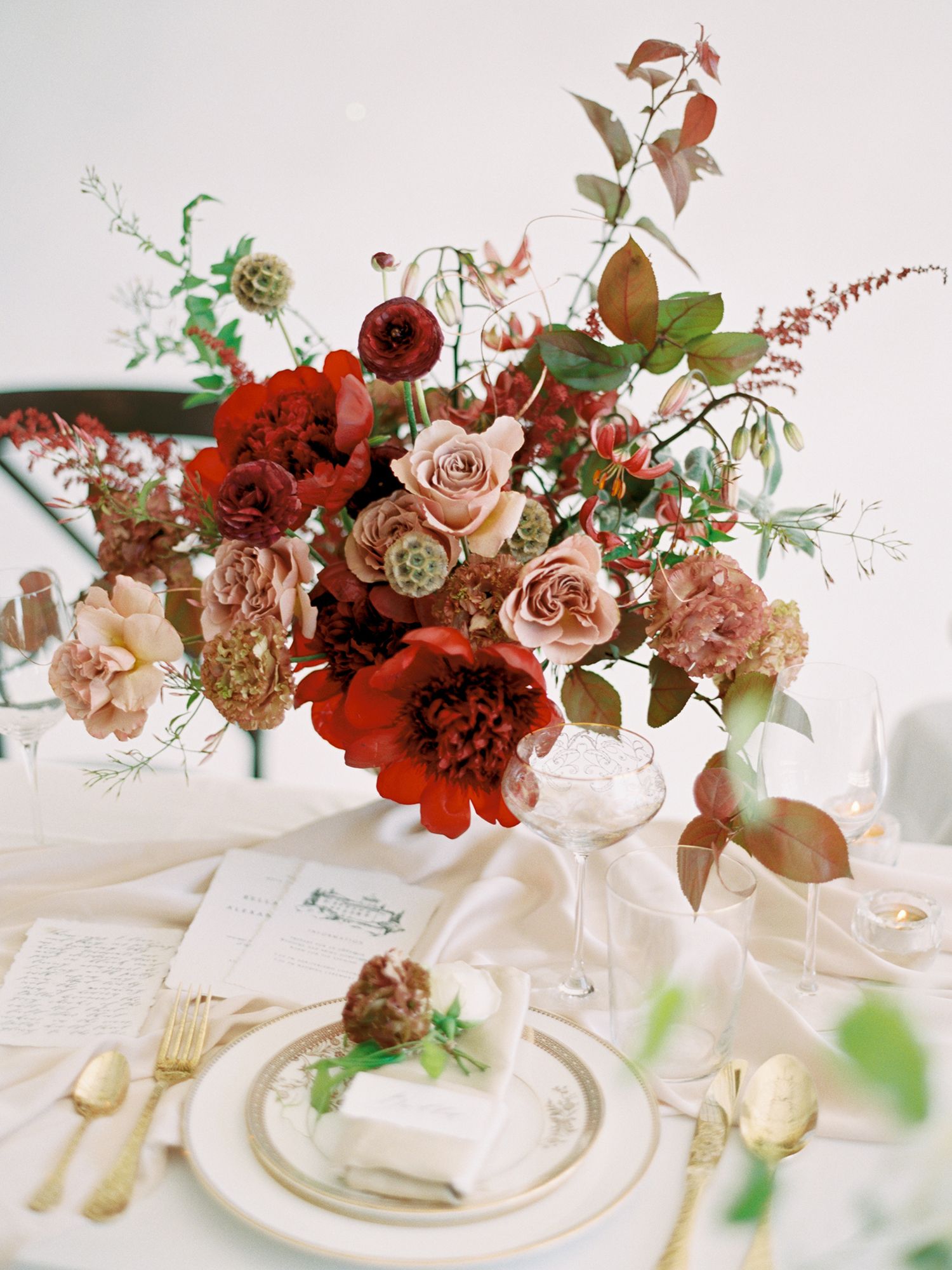 Romantic fall-colored floral centerpiece with red and blush roses on an elegant table setting.